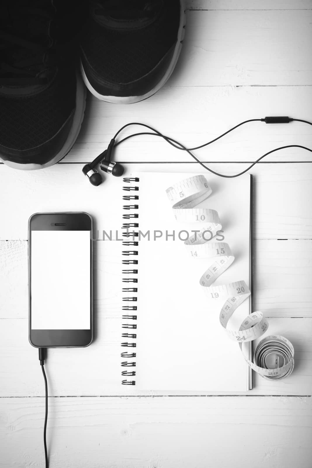 running shoes,measuring tape,notebook and phone on white wood table black and white tone color style