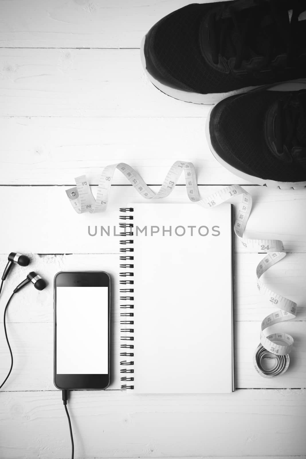 running shoes,measuring tape,notebook and phone on white wood table black and white tone color style