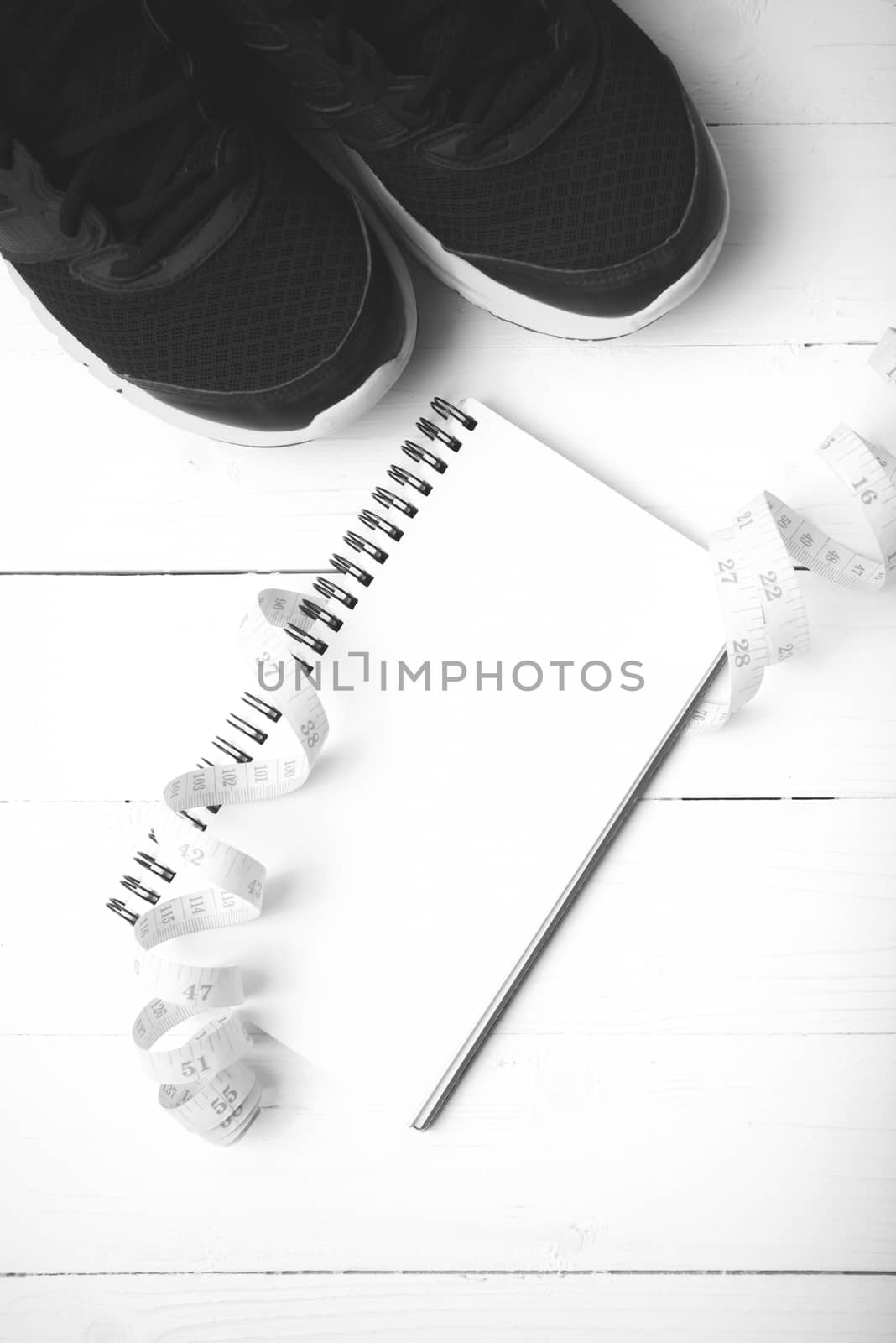 running shoes with notebook and measuring tape on white wood table black and white tone color style