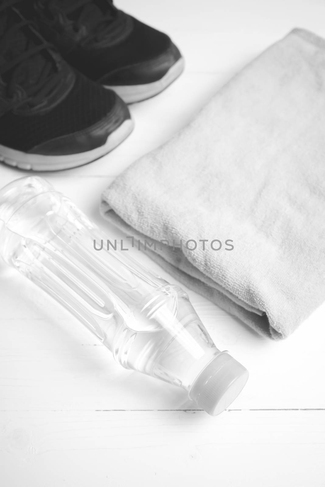 fitness equipment: towel,drinking water and running shoes on white wood table black and white color style