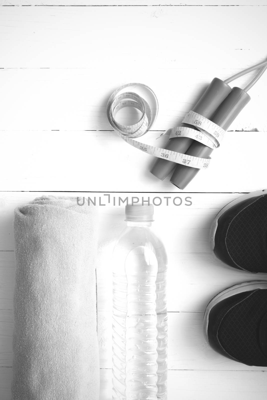 fitness equipment : running shoes,towel,jumping rope,water bottle and measuring tape on white wood table black and white color tone style