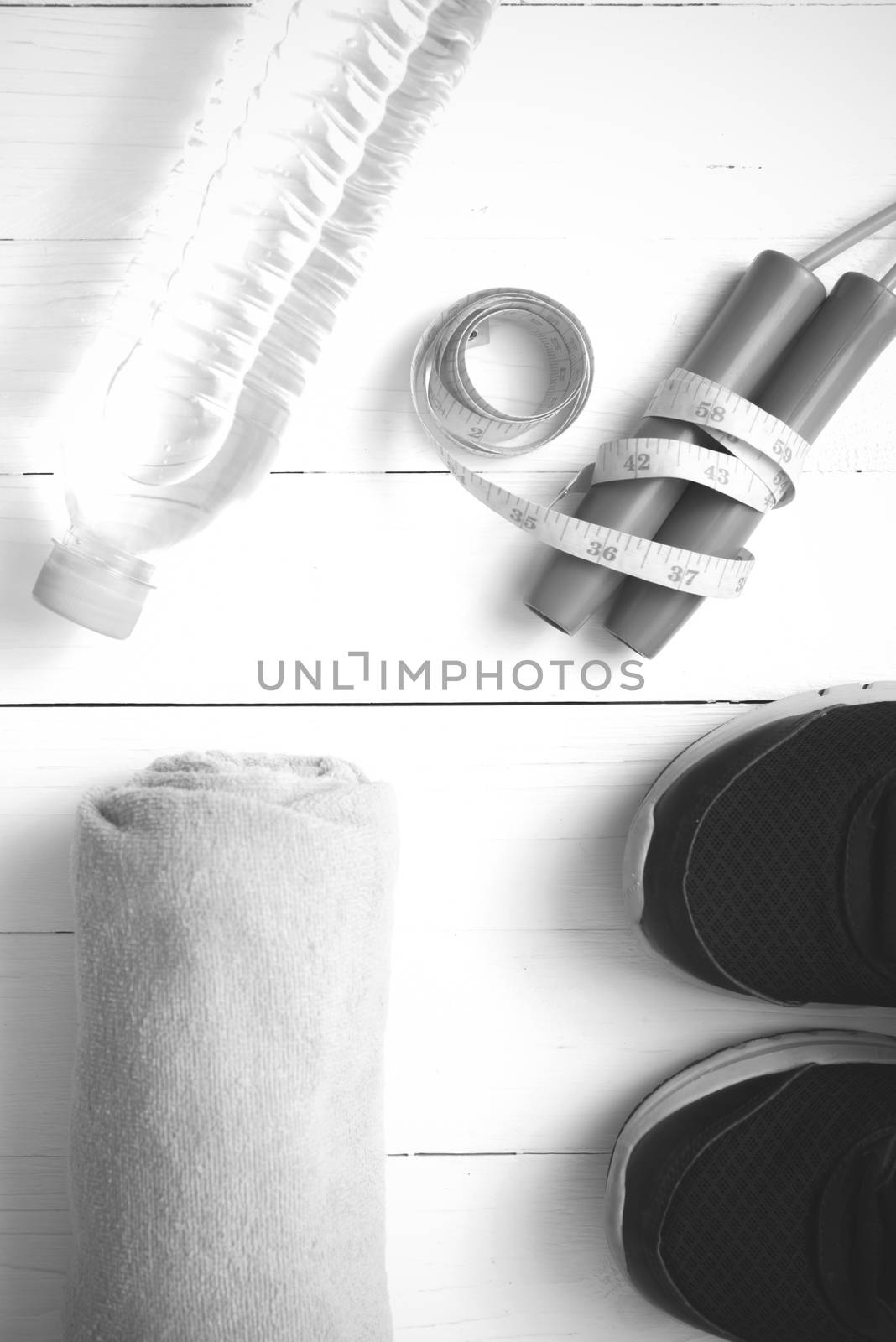 fitness equipment : running shoes,towel,jumping rope,water bottle and measuring tape on white wood table black and white color tone style