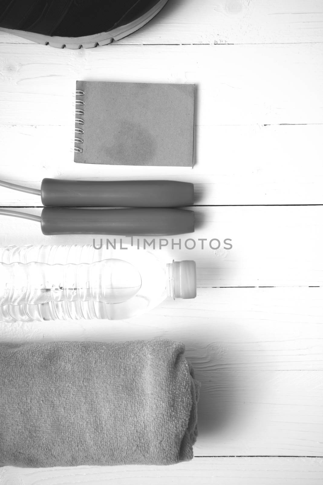 fitness equipment : running shoes,towel,jumping rope,water bottle and notepad on white wood table black and white color tone style