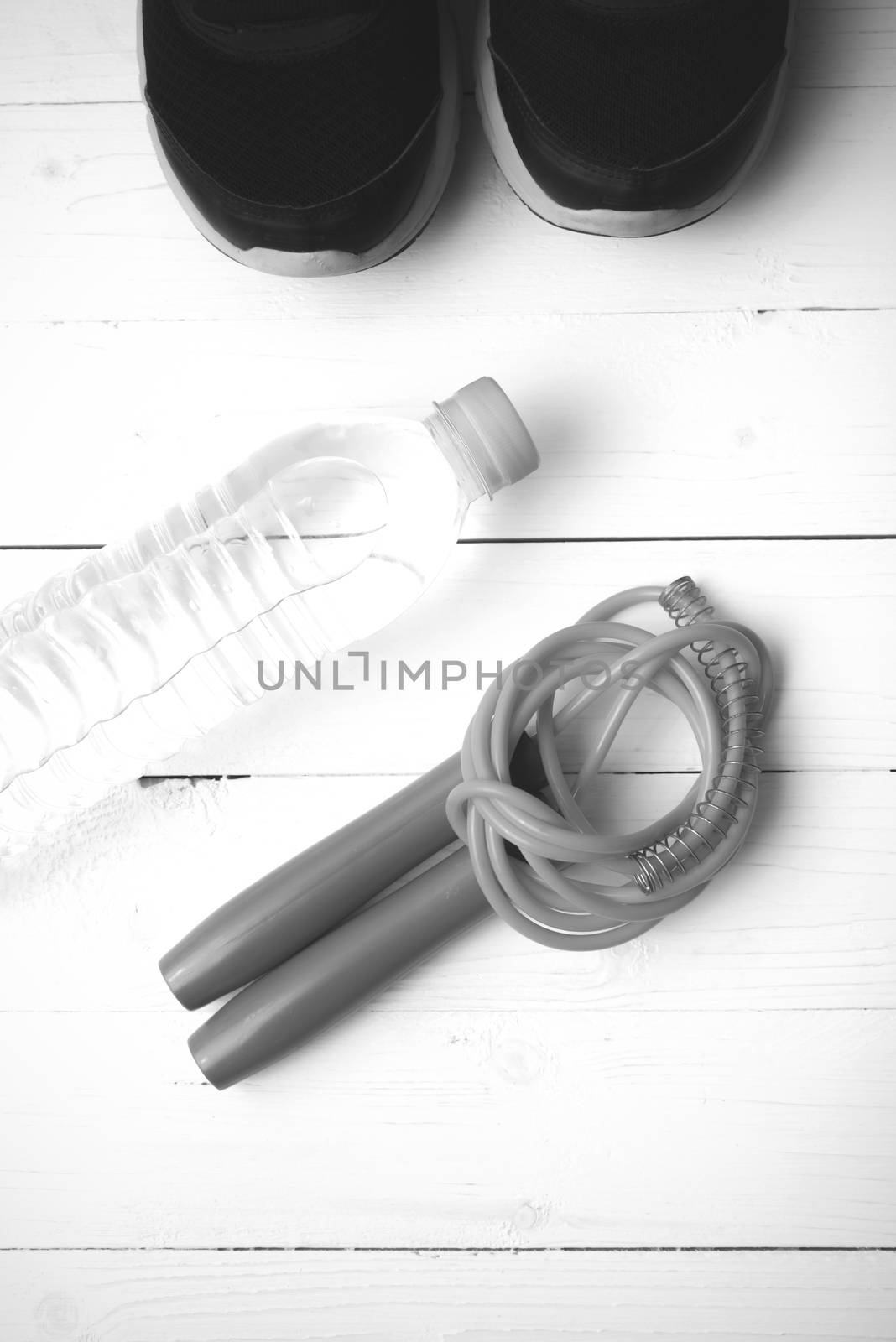 fitness equipment : running shoes,jumping rope and water bottle on white wood table black and white color tone style