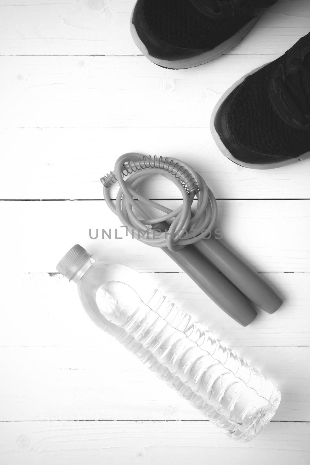 fitness equipment : running shoes,jumping rope and water bottle on white wood table black and white color tone style