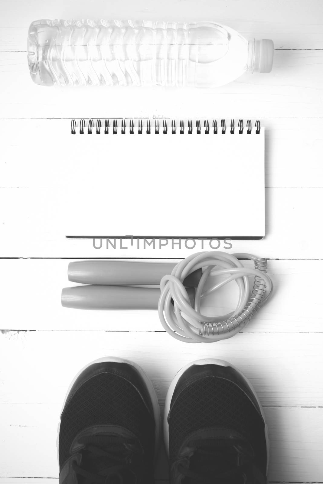 fitness equipment : running shoes,jumping rope,drinking water and notepad on white wood table  black and white tone color style