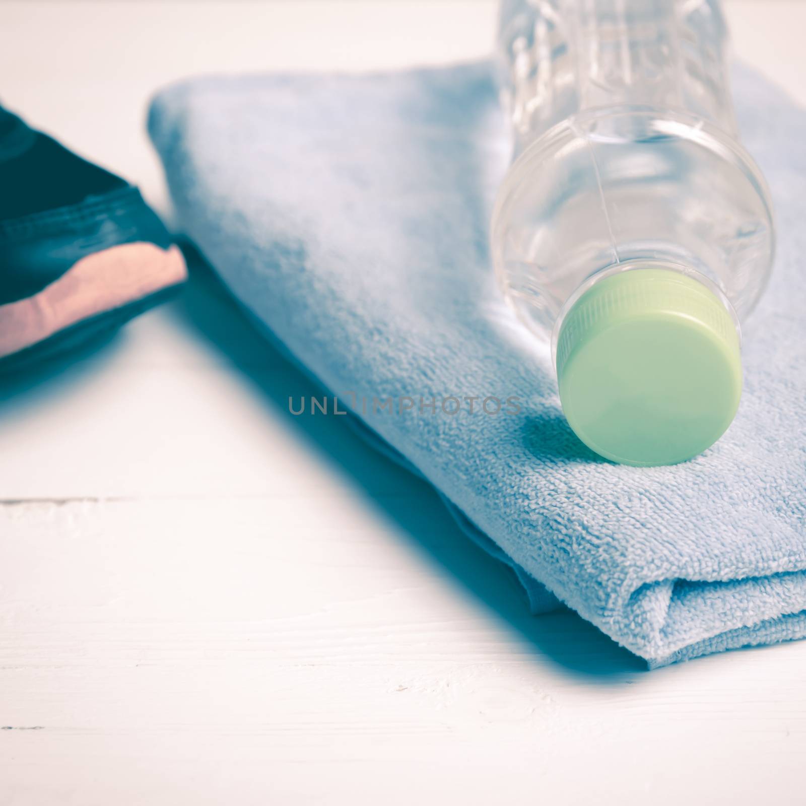 fitness equipment:blue towel,drinking water and running shoes on white wood table vintage style