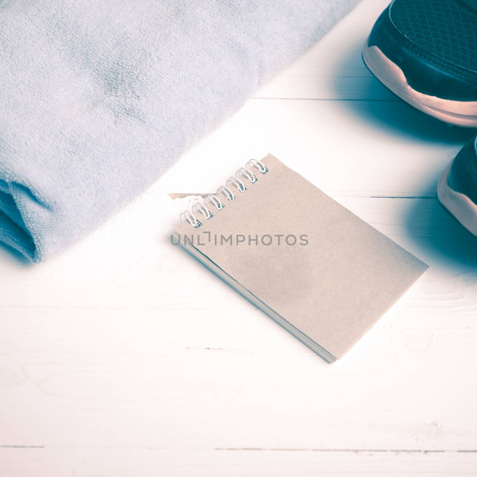 fitness equipment : running shoes,blue towel and notepad on white wood table vintage style