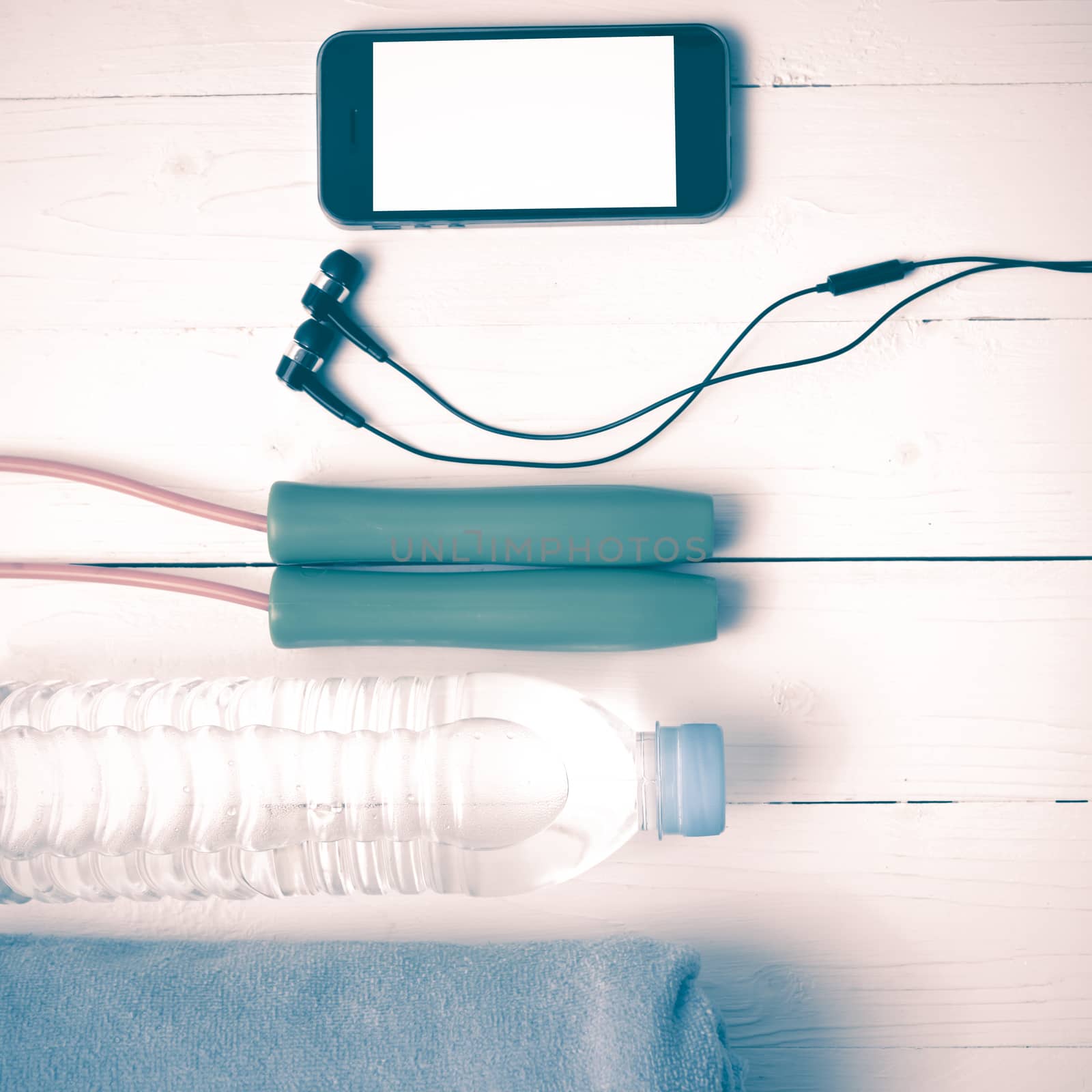 fitness equipment :towel,jumping rope,water bottle and phone on white wood table vintage style