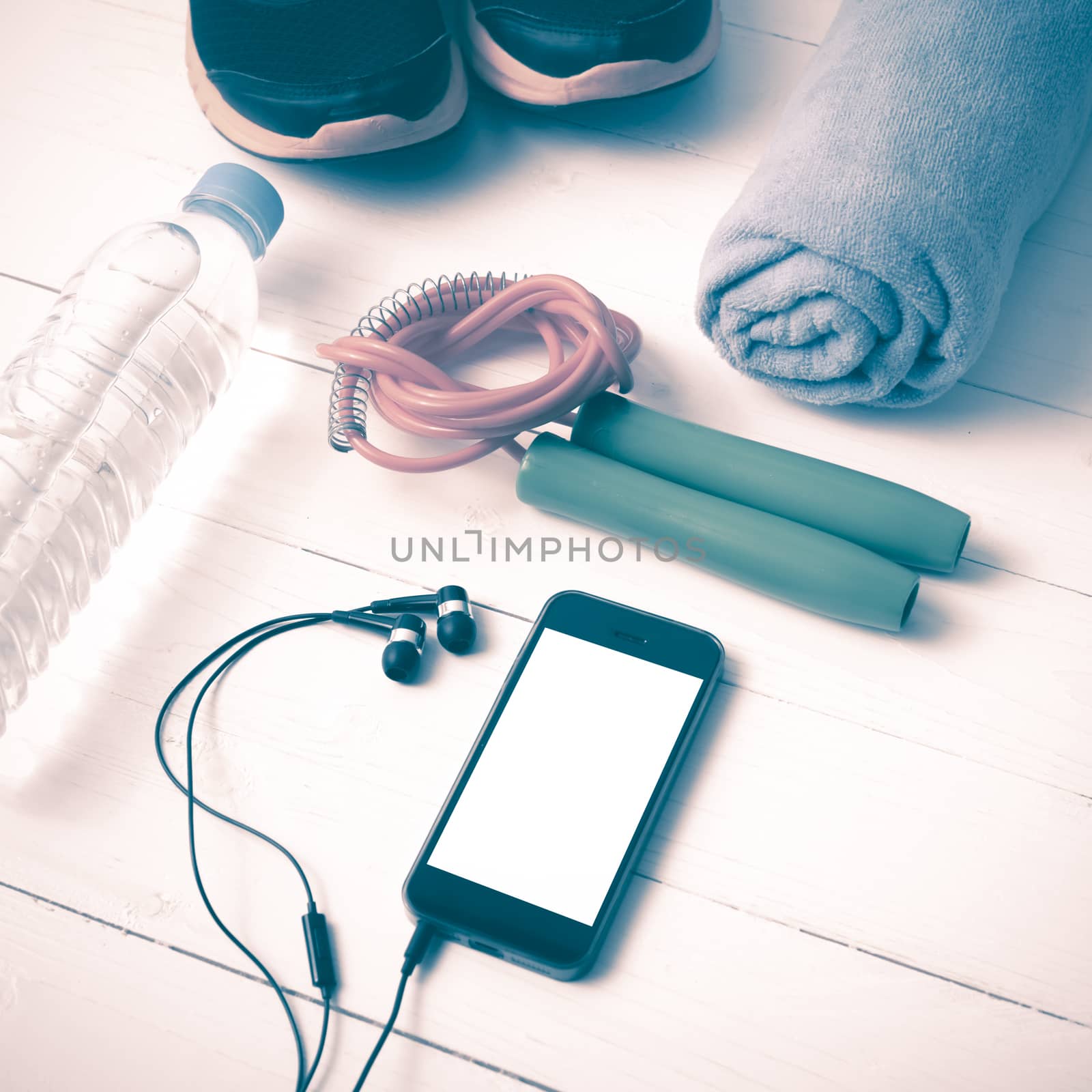 fitness equipment : running shoes,towel,jumping rope,water bottle and phone on white wood table vintage style