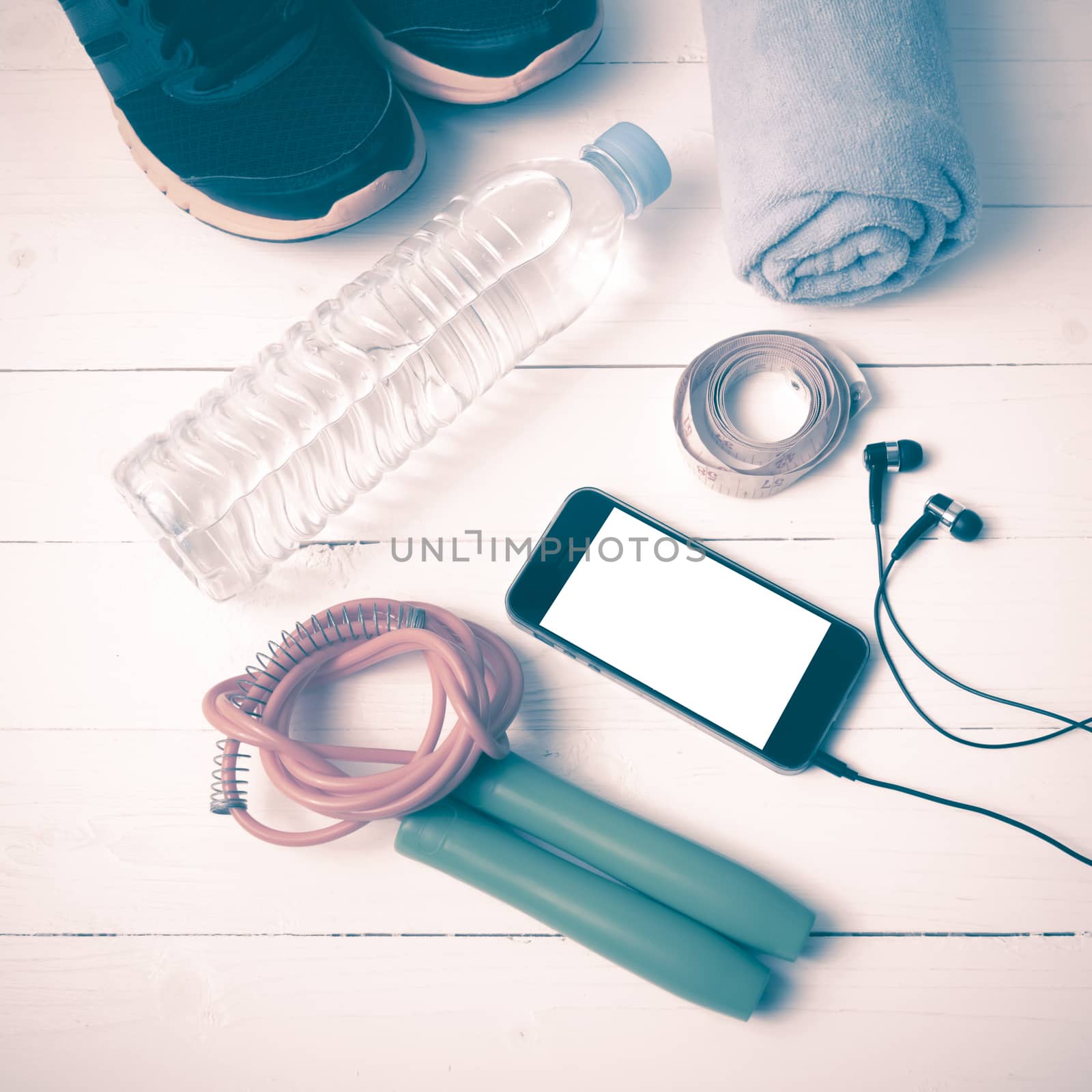 fitness equipment : running shoes,towel,jumping rope,water bottle,phone and measuring tape on white wood table vintage style