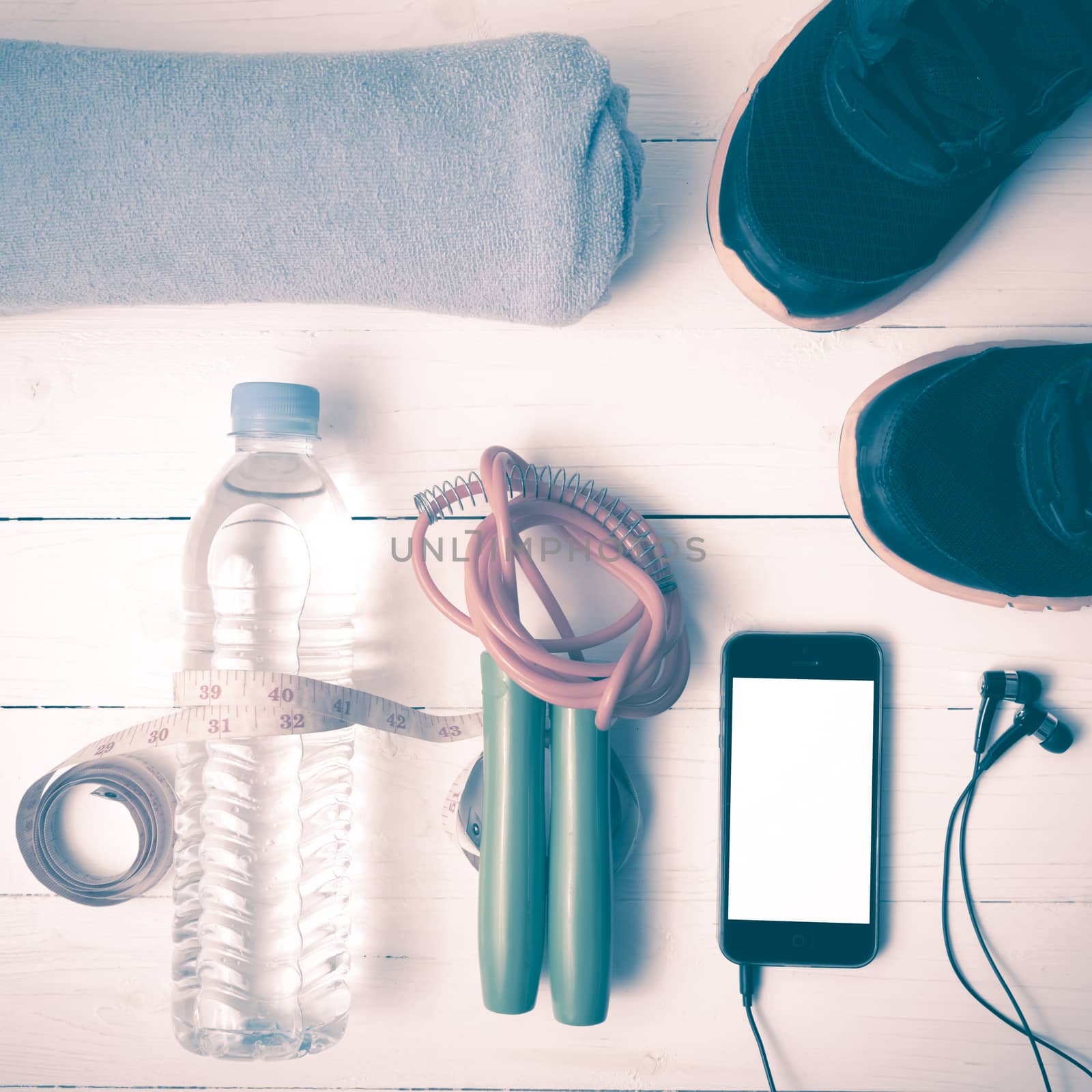 fitness equipment : running shoes,towel,jumping rope,water bottle,phone and measuring tape on white wood table vintage style