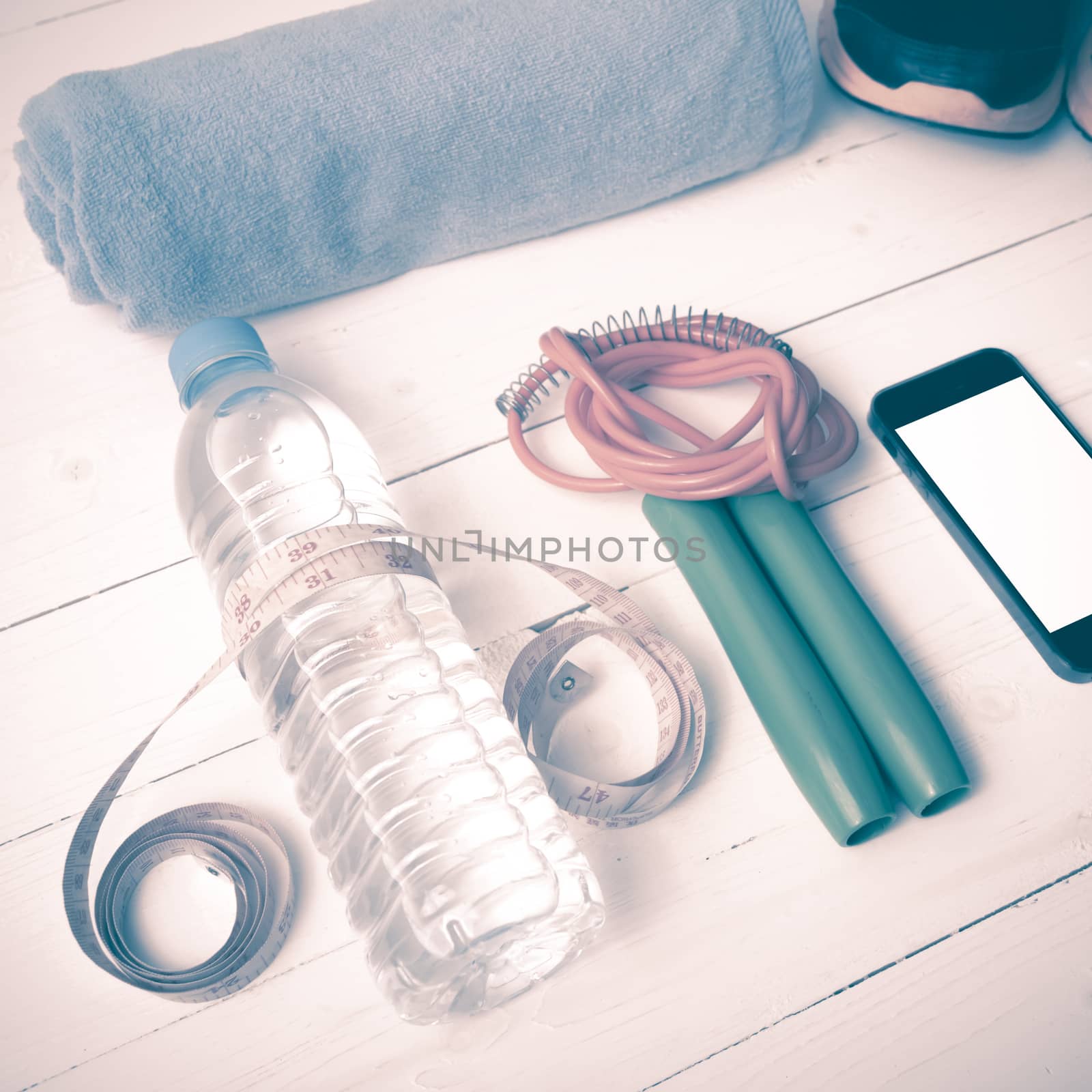 fitness equipment : running shoes,towel,jumping rope,water bottle,phone and measuring tape on white wood table vintage style