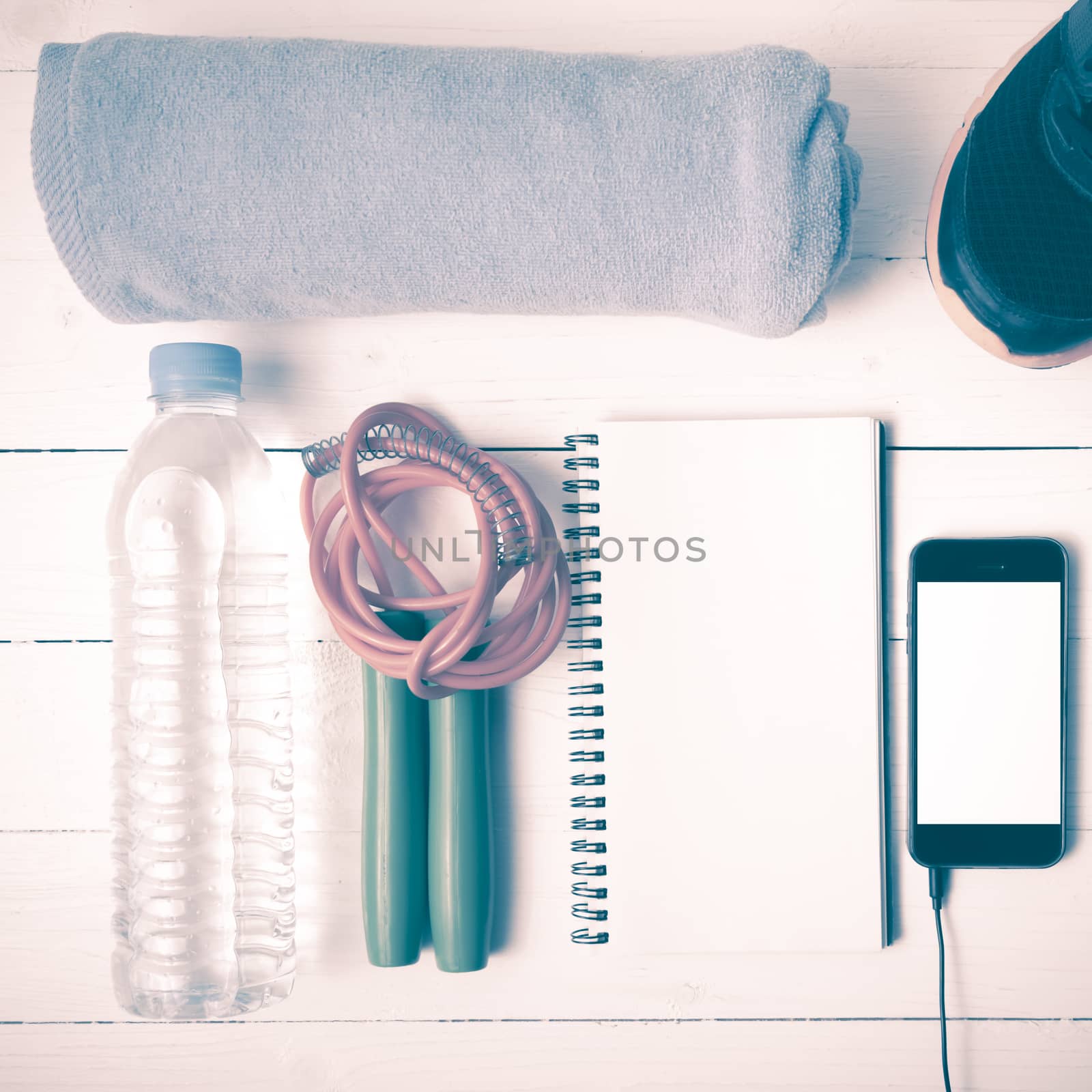 fitness equipment : running shoes,towel,jumping rope,water bottle,phone and notepad on white wood table vintage style