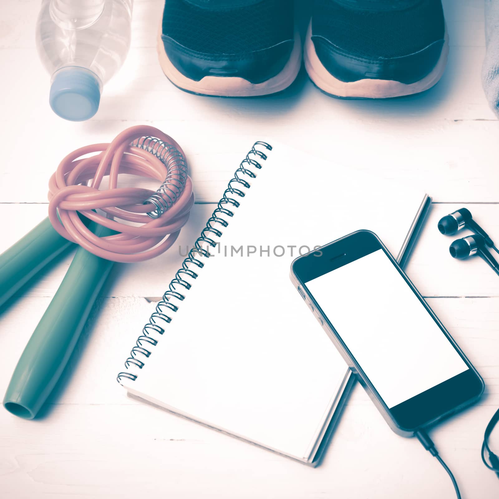 fitness equipment : running shoes,towel,jumping rope,water bottle,phone and notepad on white wood table vintage style