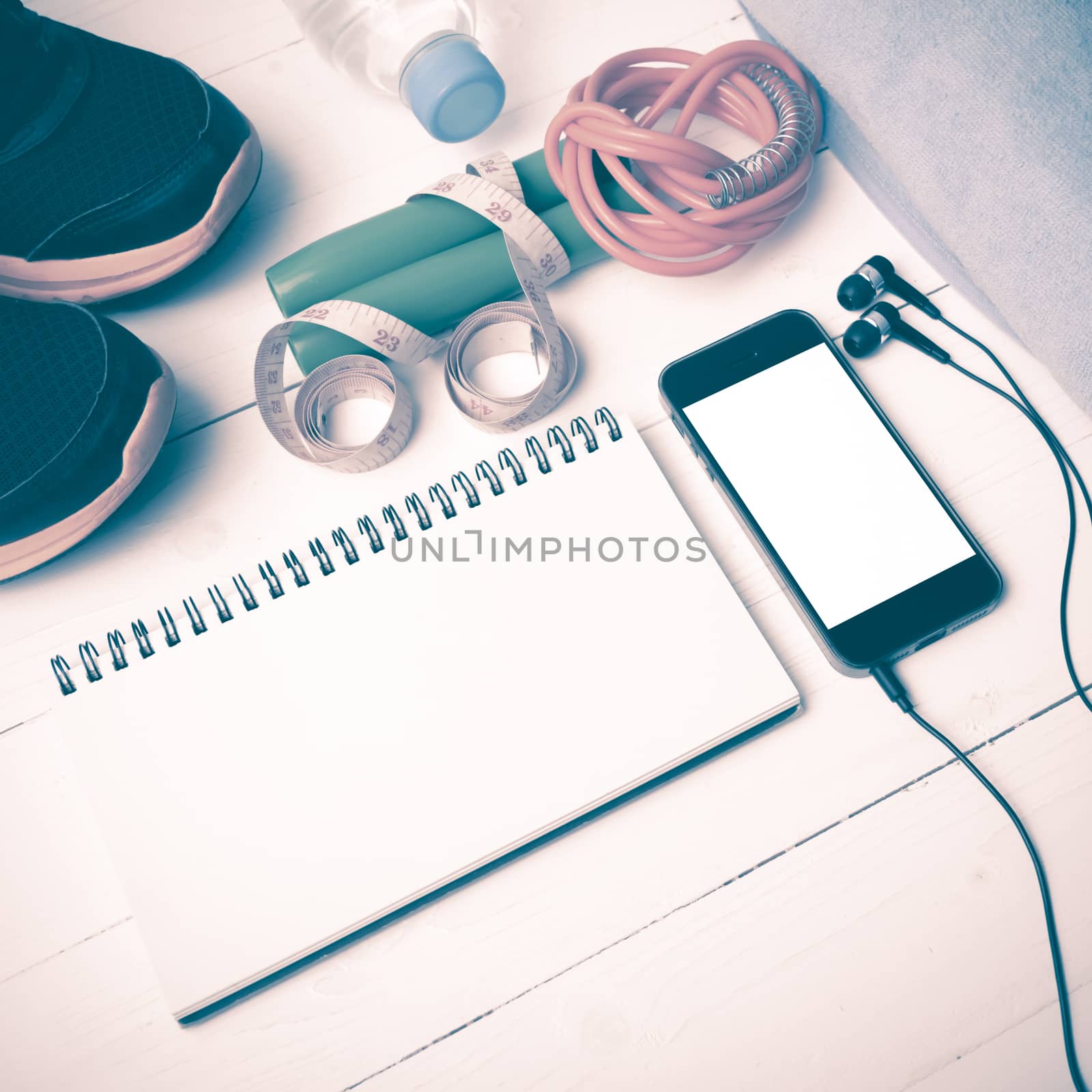 fitness equipment : running shoes,towel,jumping rope,water bottle,phone,notepad and measuring tape on white wood table vintage style