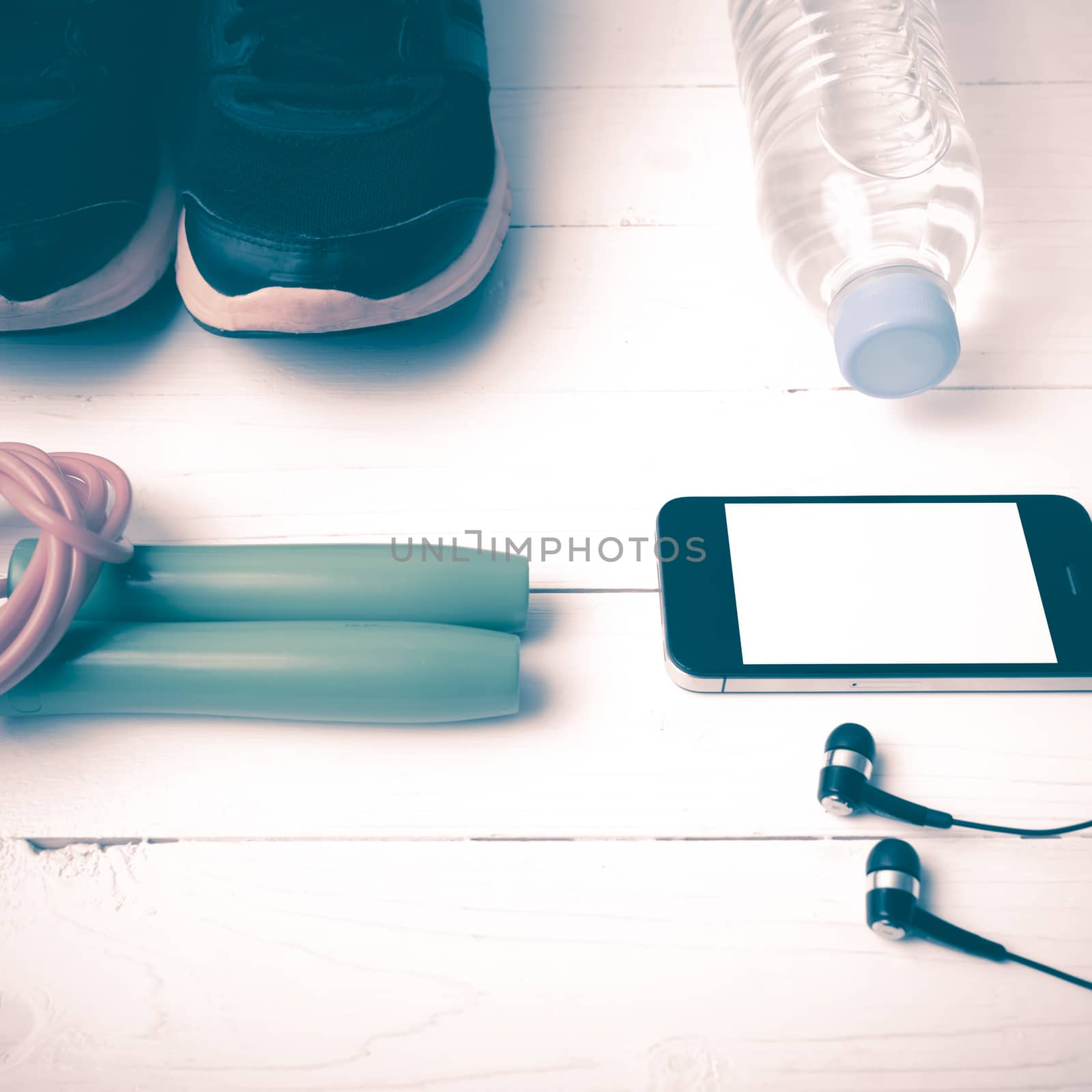 fitness equipment : running shoes,jumping rope,phone and water bottle on white wood table vintage style