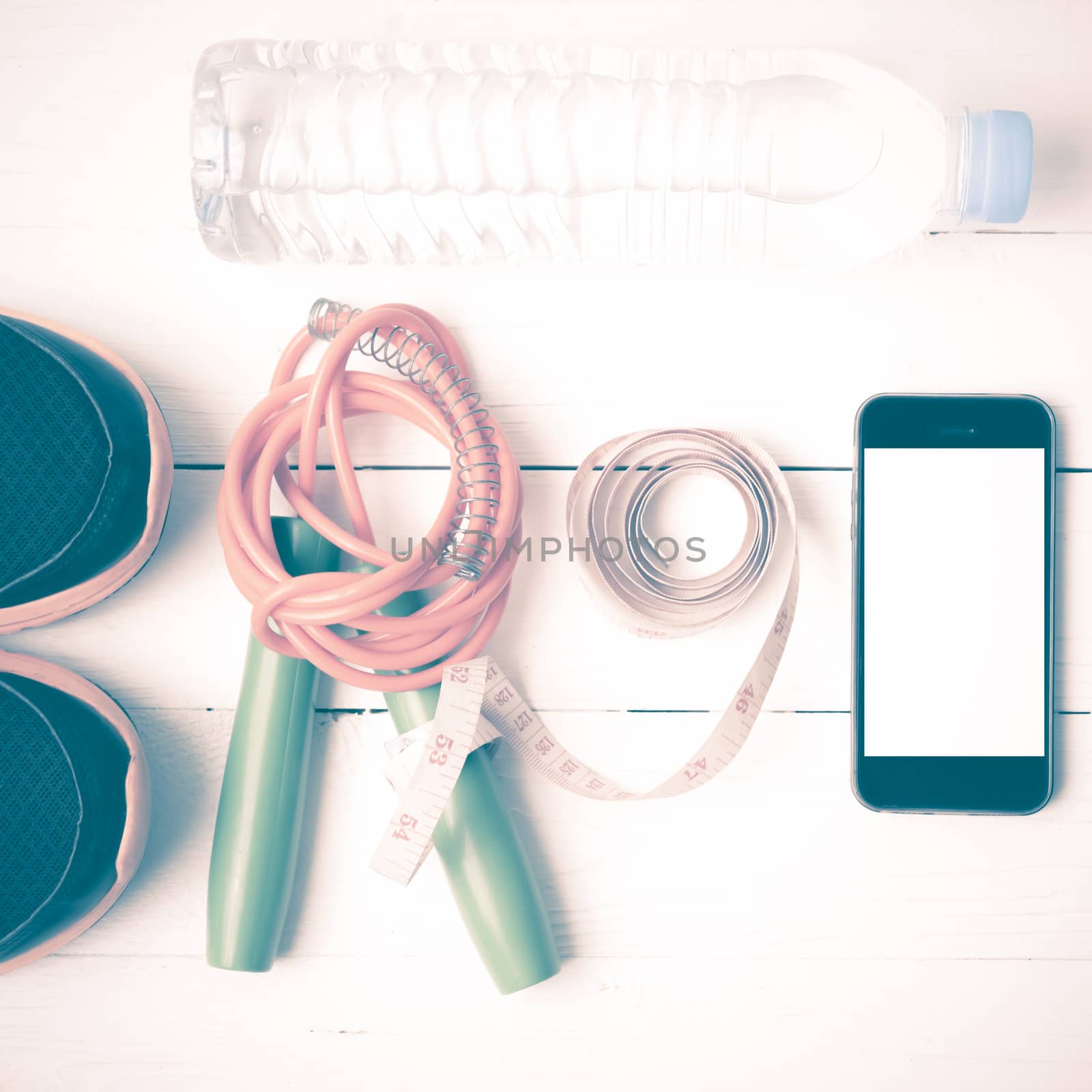 fitness equipment : running shoes,jumping rope,drinking water,measuring tape and phone on white wood table vintage style