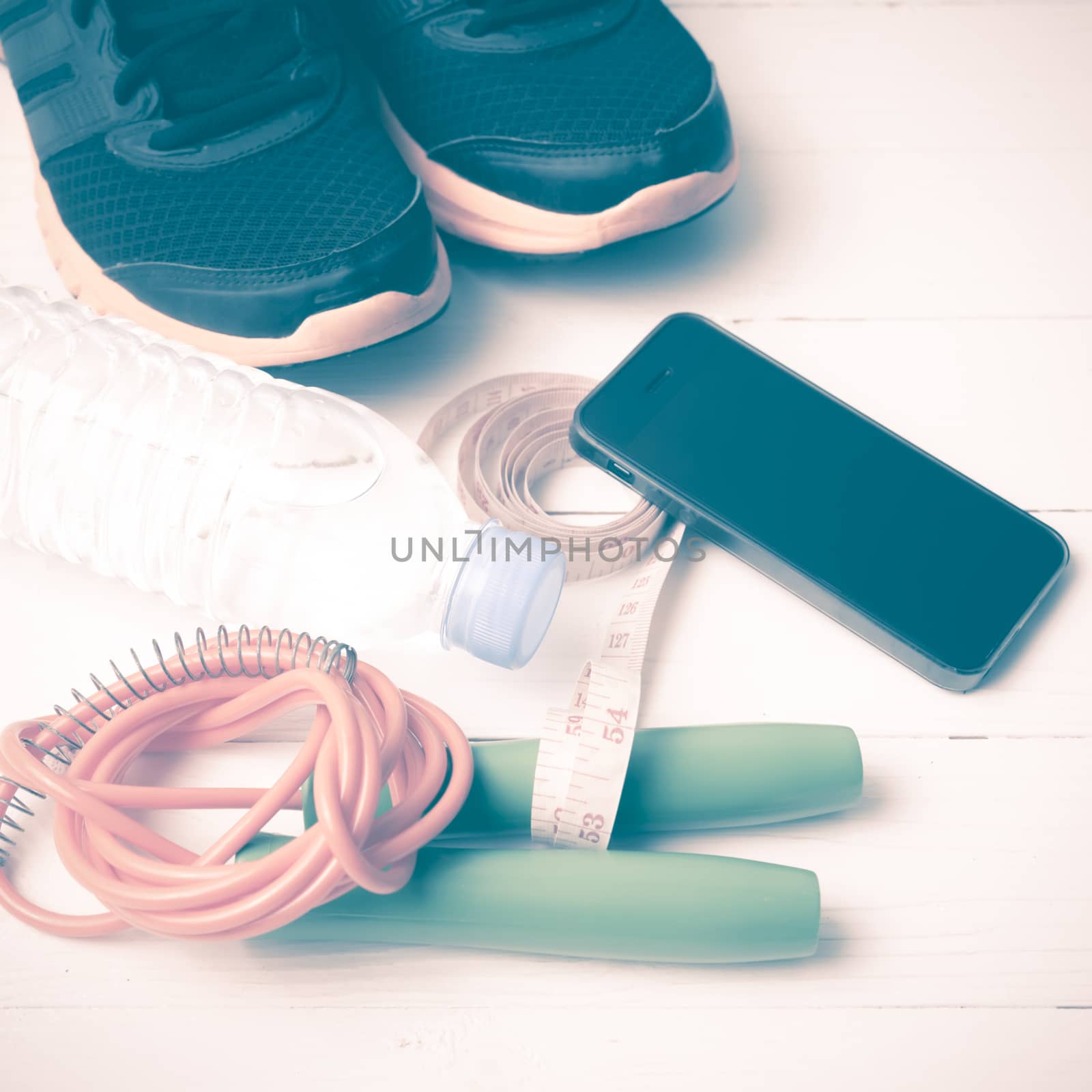 fitness equipment : running shoes,jumping rope,drinking water,measuring tape and phone on white wood table vintage style