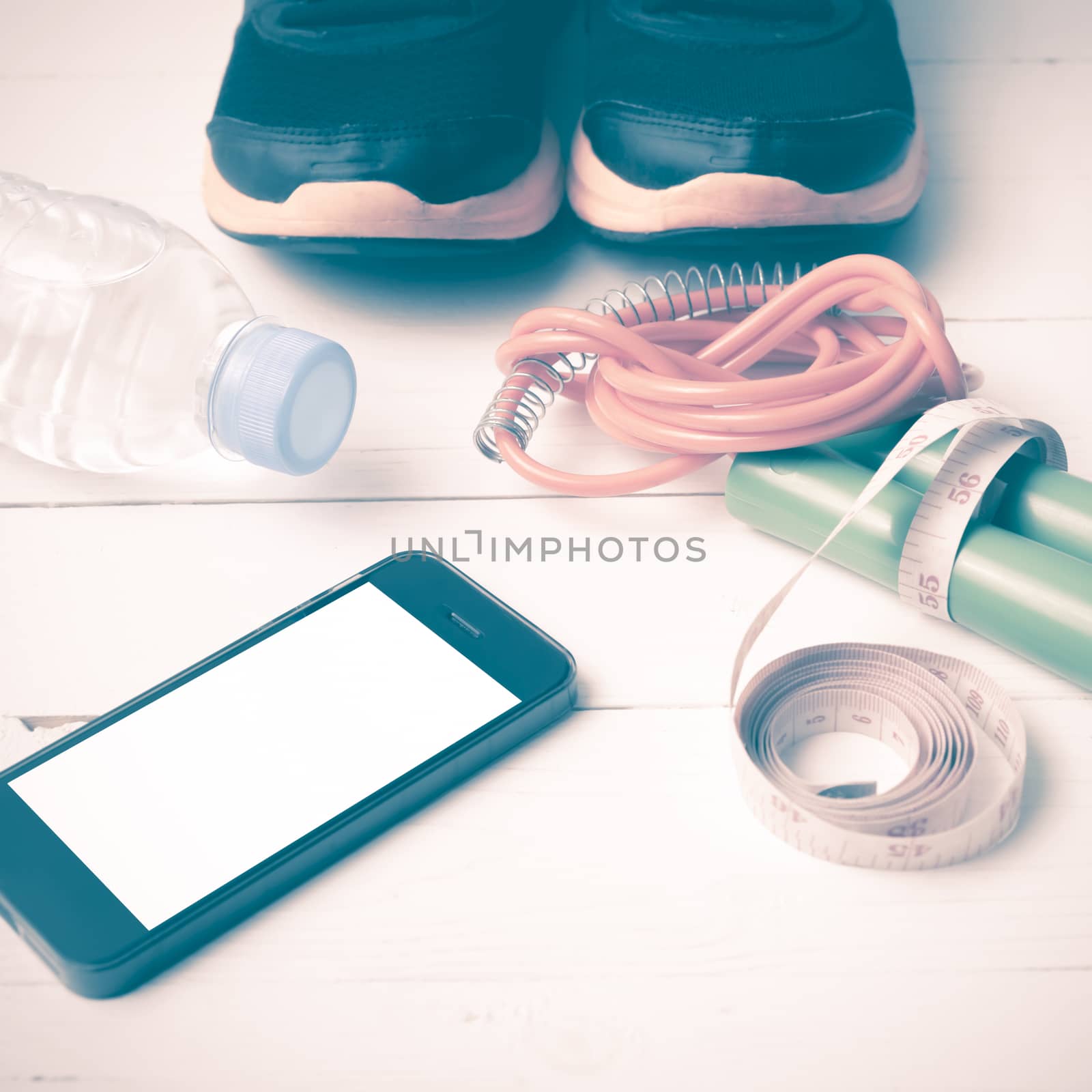 fitness equipment : running shoes,jumping rope,drinking water,measuring tape and phone on white wood table vintage style