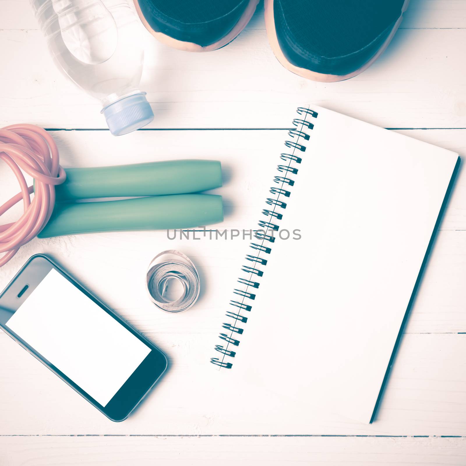 fitness equipment : running shoes,jumping rope,drinking water,notebook,measuring tape and phone on white wood table vintage style