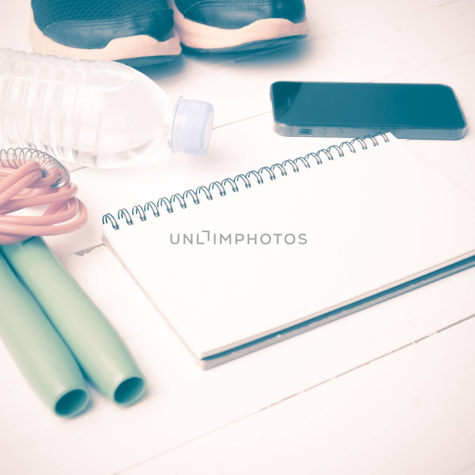 fitness equipment : running shoes,jumping rope,drinking water,notebook and phone on white wood table vintage style