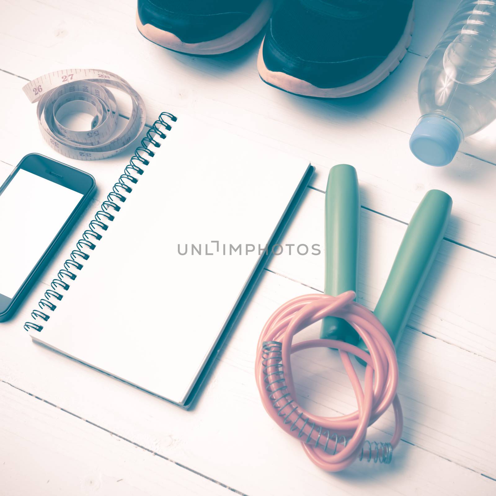 fitness equipment : running shoes,jumping rope,drinking water,notebook,measuring tape and phone on white wood table vintage style