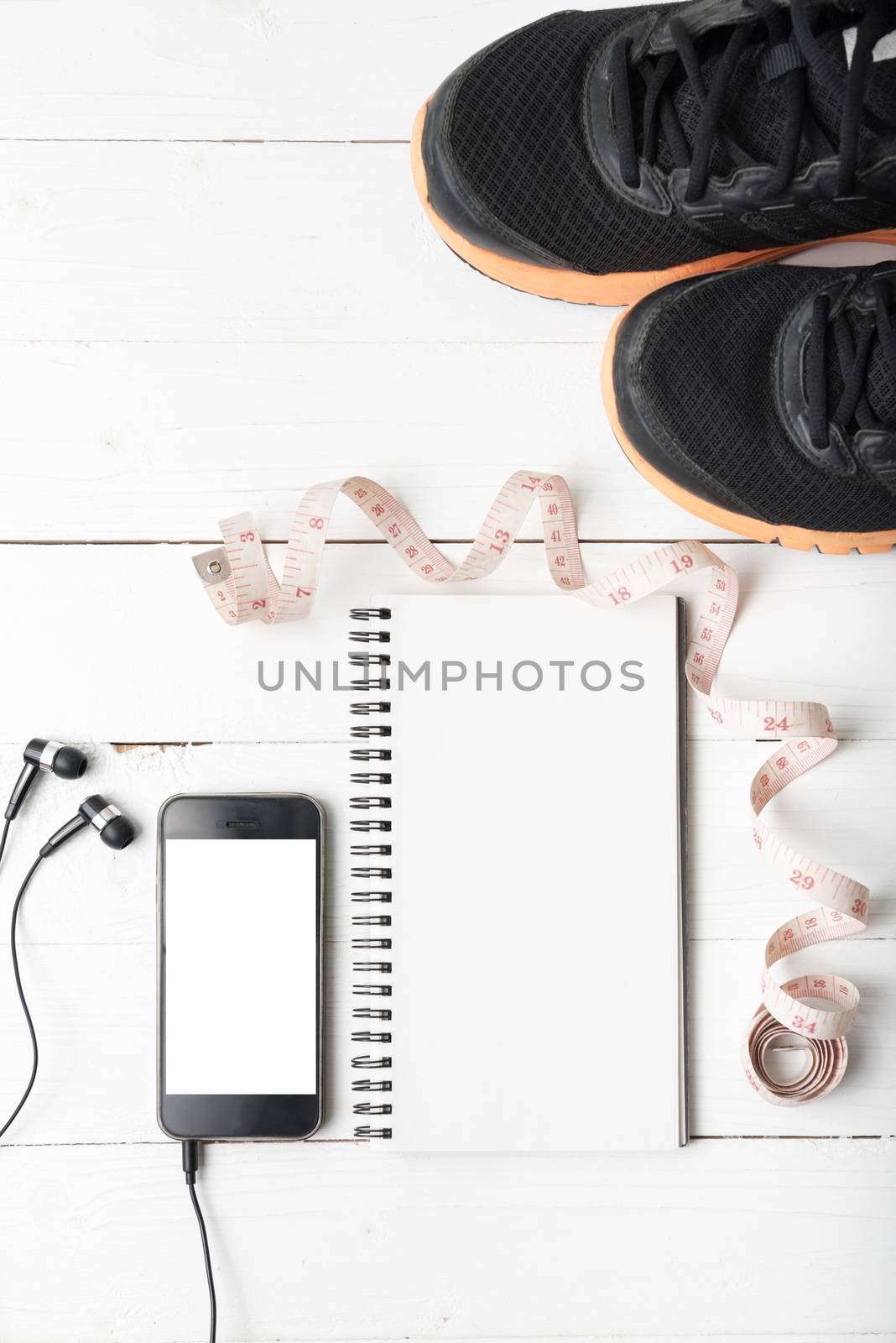 running shoes,measuring tape,notebook and phone on white wood table