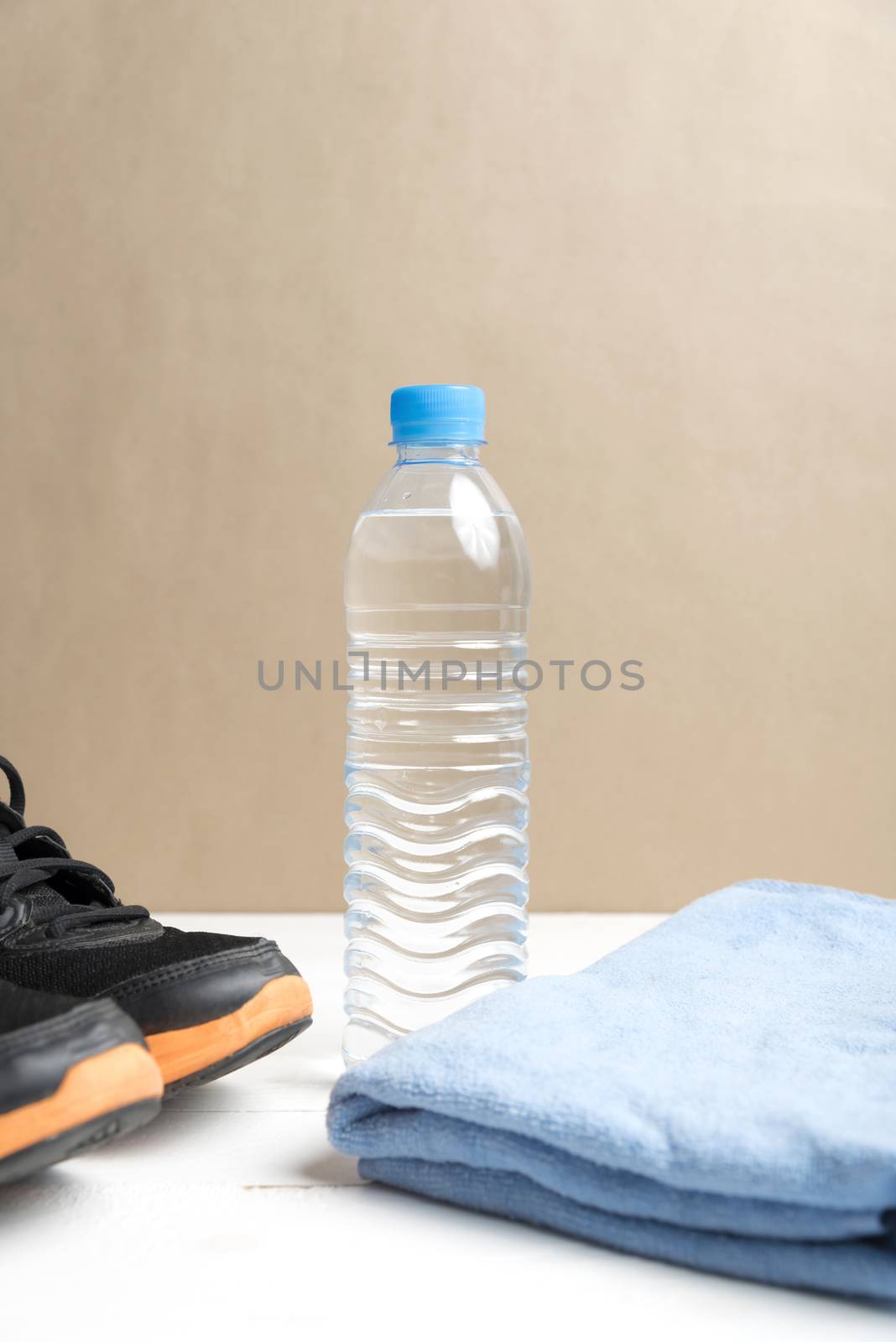 fitness equipment:blue towel,drinking water and running shoes on white wood table