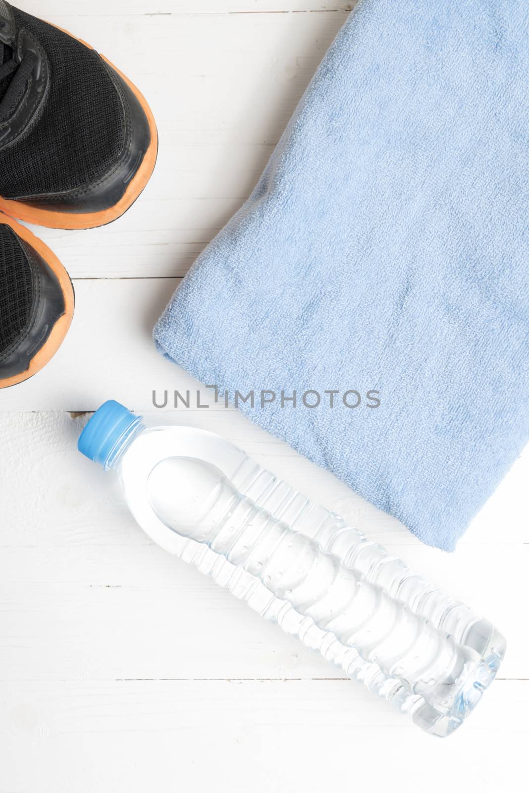 fitness equipment:blue towel,drinking water and running shoes on white wood table