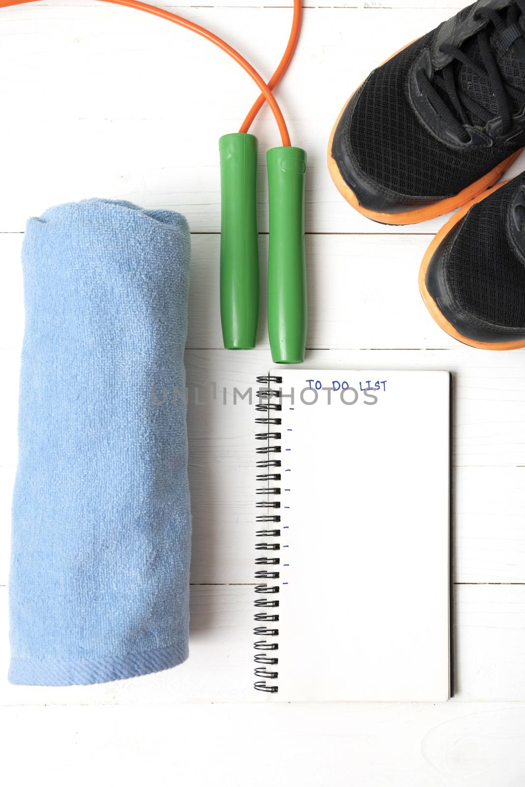 fitness equipment : running shoes,towel,jumping rope and notebook write to do list on white wood table