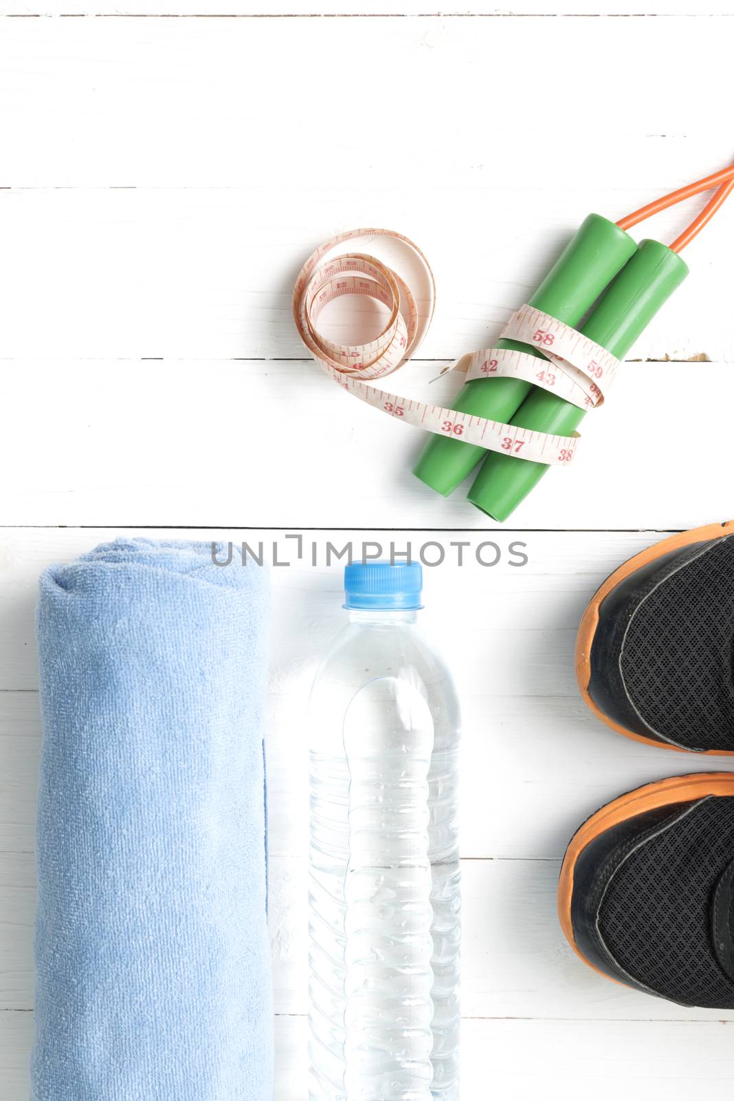 fitness equipment : running shoes,towel,jumping rope,water bottle and measuring tape on white wood table