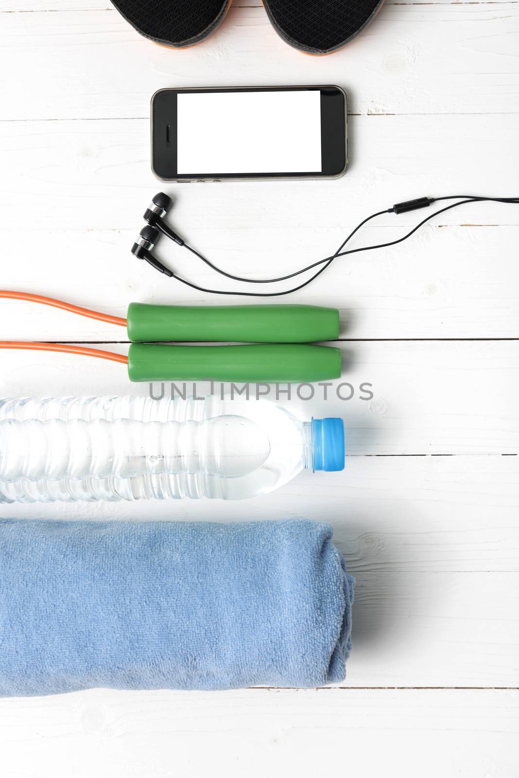 fitness equipment : running shoes,towel,jumping rope,water bottle and phone on white wood table