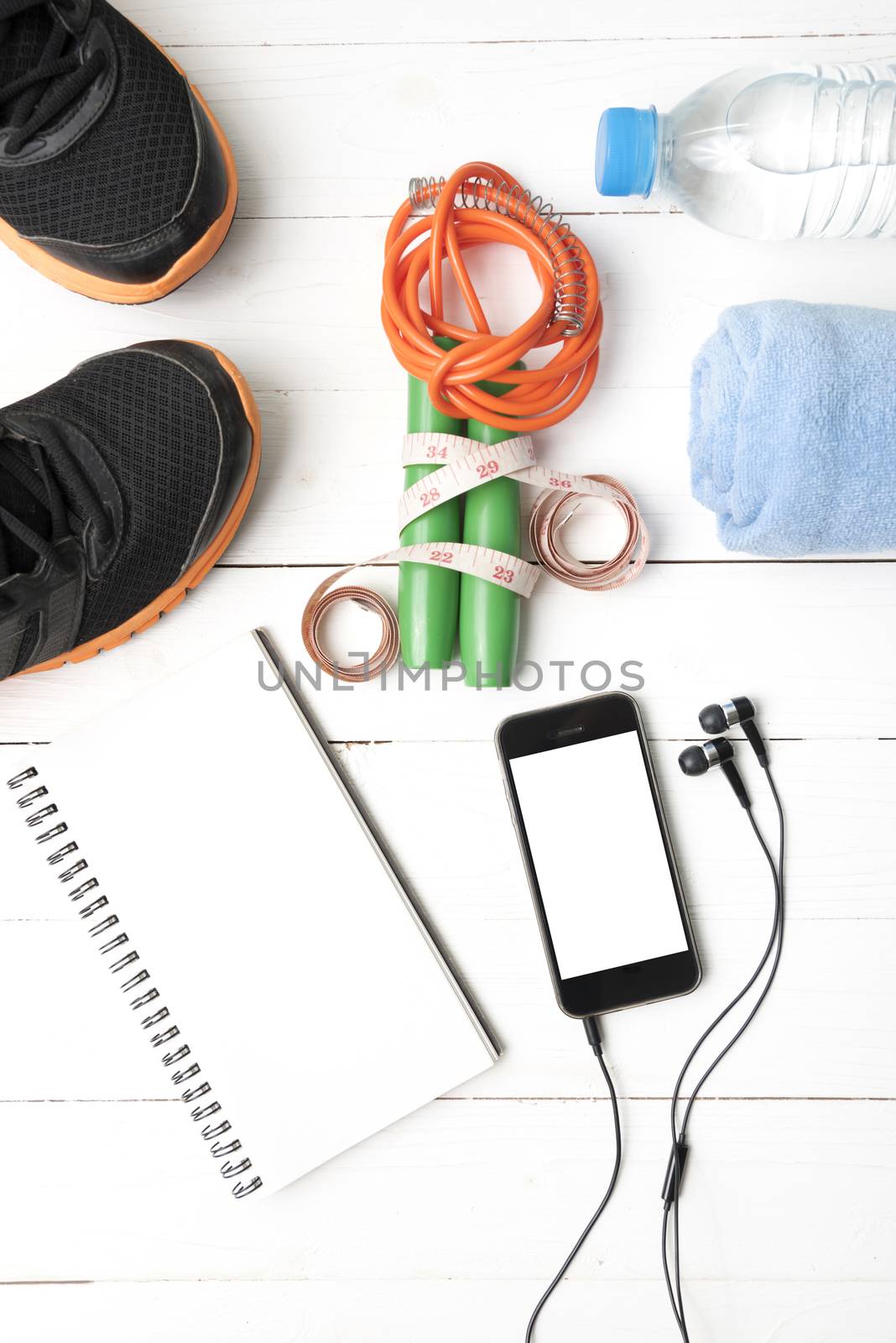 fitness equipment : running shoes,towel,jumping rope,water bottle,phone,notepad and measuring tape on white wood table