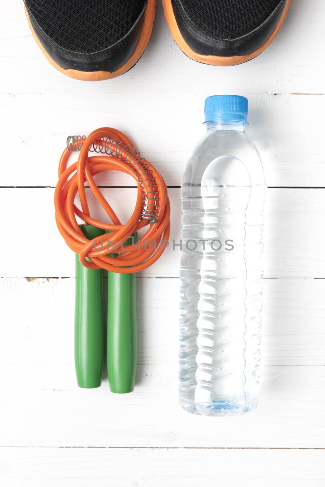 fitness equipment : running shoes,jumping rope and water bottle on white wood table