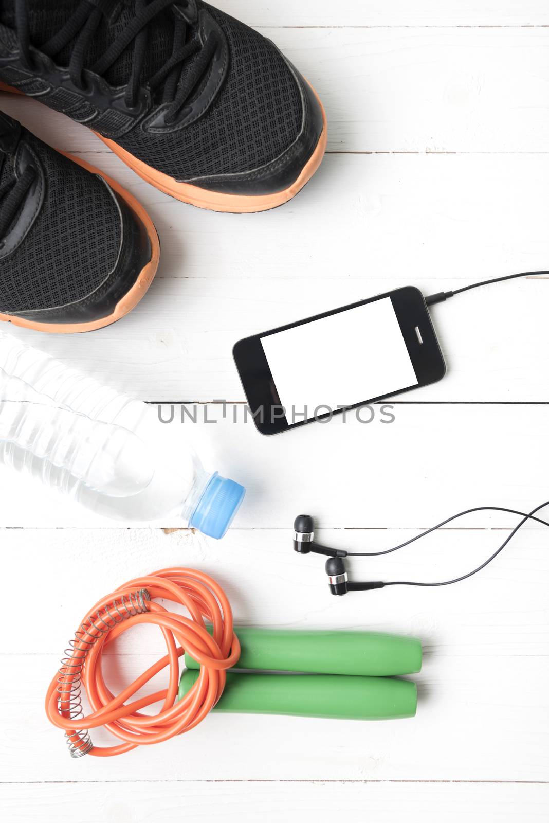 fitness equipment : running shoes,jumping rope,phone and water bottle on white wood table