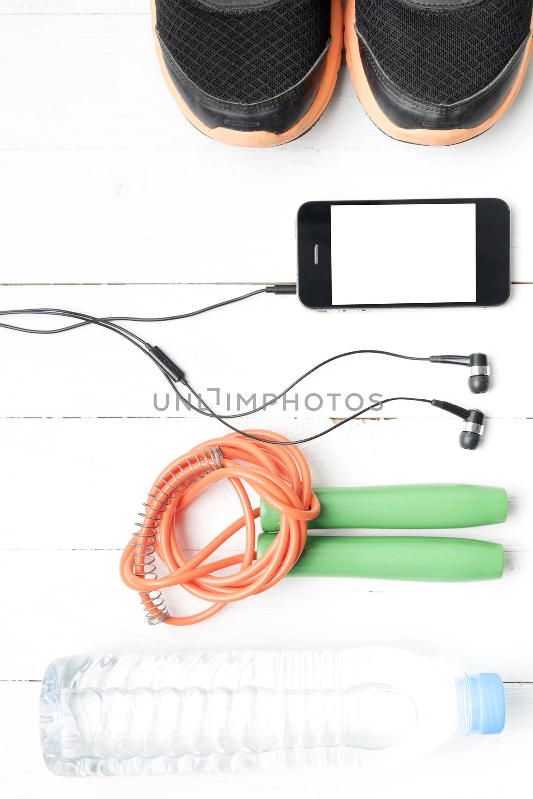 fitness equipment : running shoes,jumping rope,phone and water bottle on white wood table
