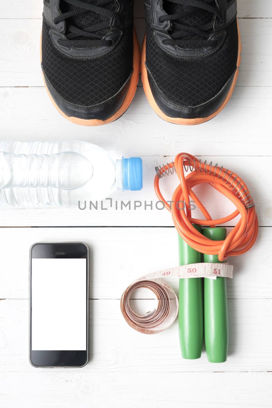 fitness equipment : running shoes,jumping rope,drinking water,measuring tape and phone on white wood table