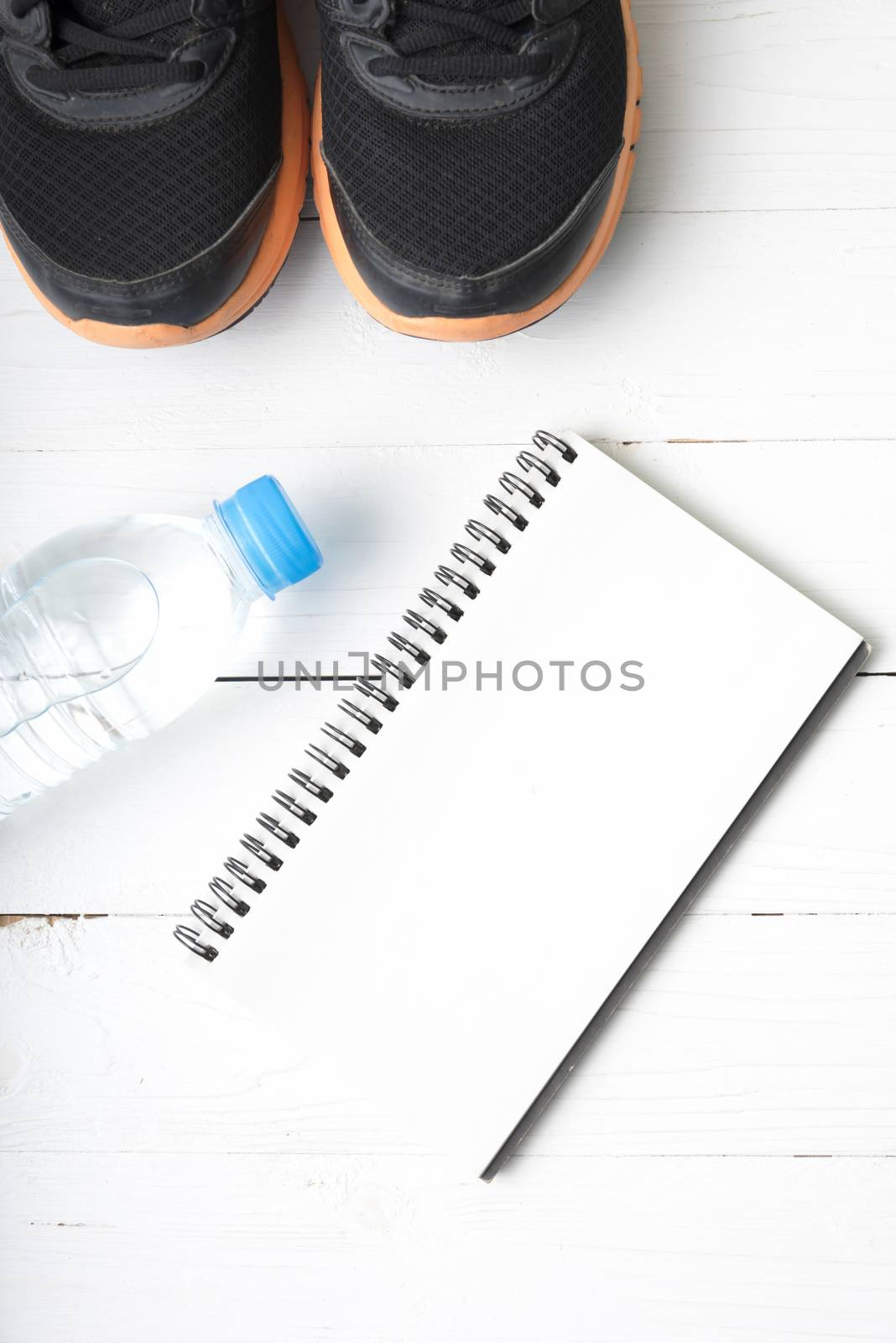 fitness equipment : running shoes,drinking water and notebook on white wood table