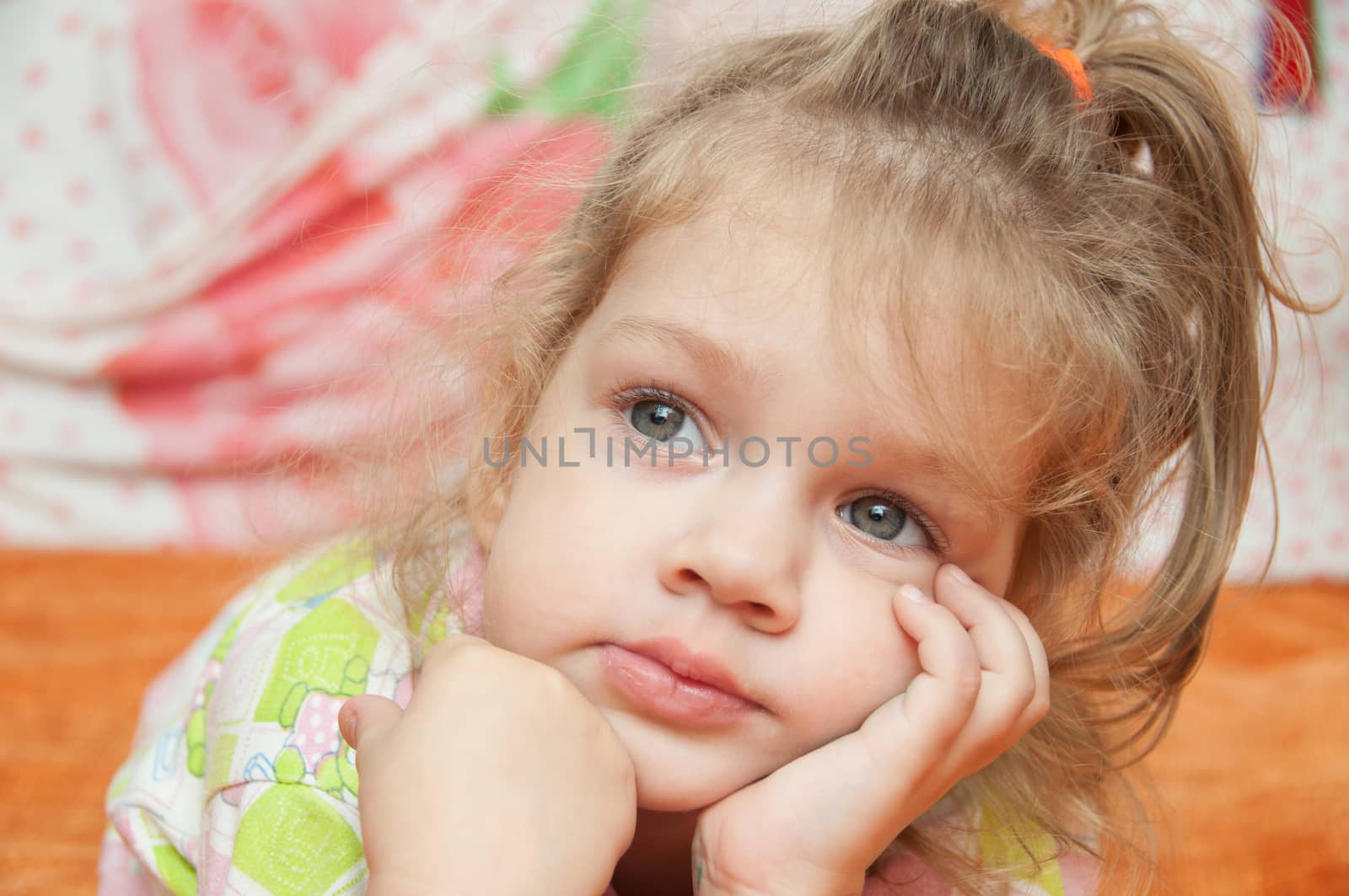 Cheerful three year old girl lying on the bed and looked to the left 