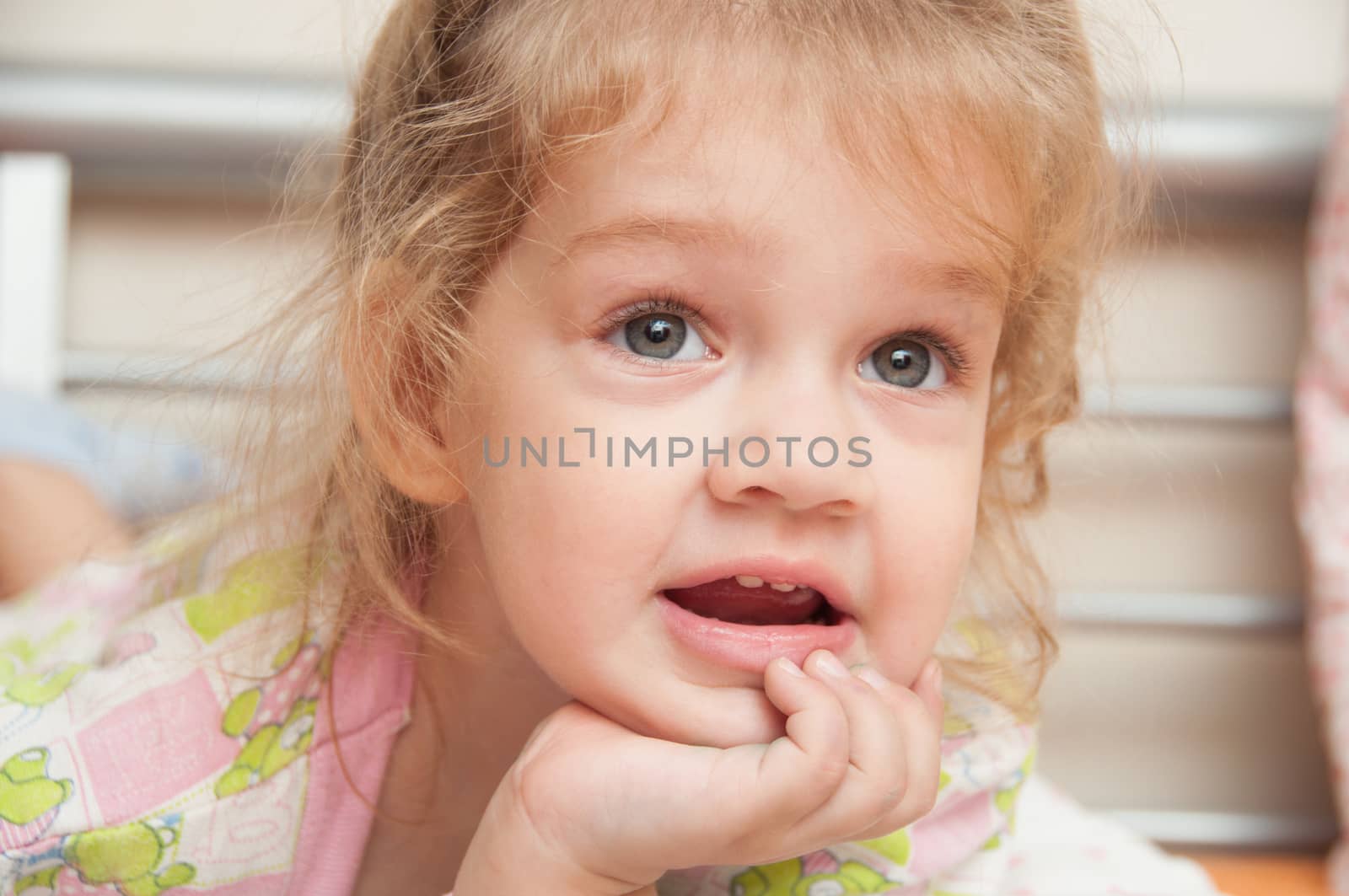 Cheerful three year old girl lying on the bed and looked past the frame 