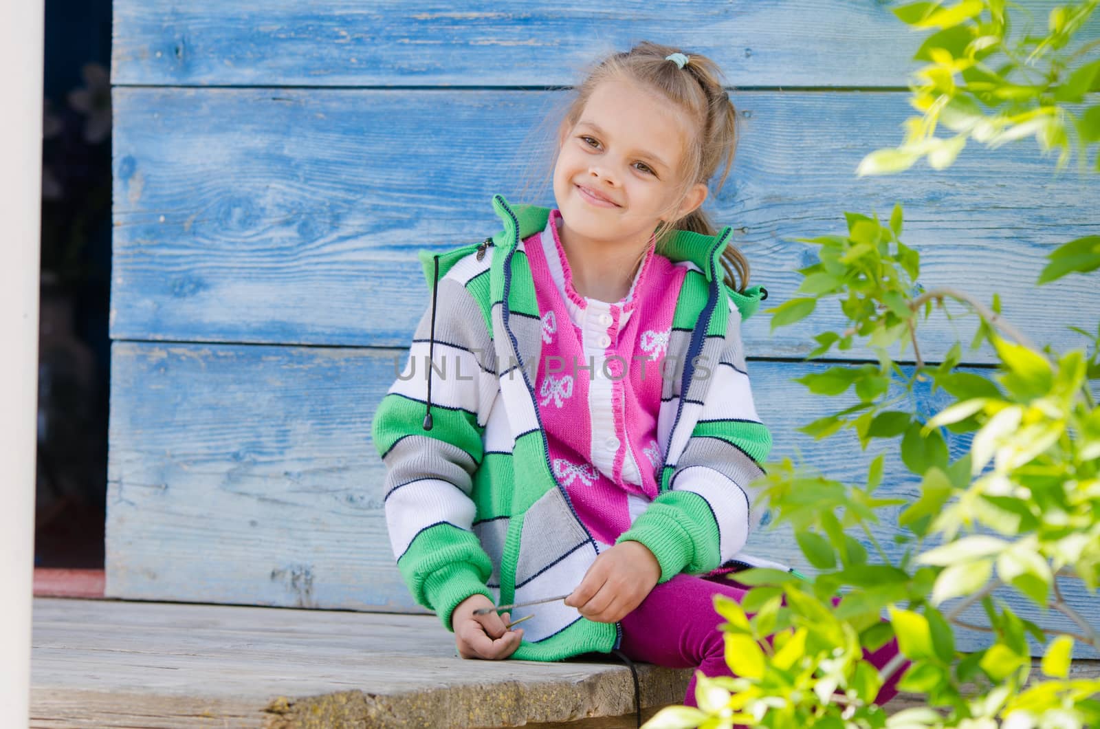 Six year old girl sitting on the porch of a wooden house and smiling happily