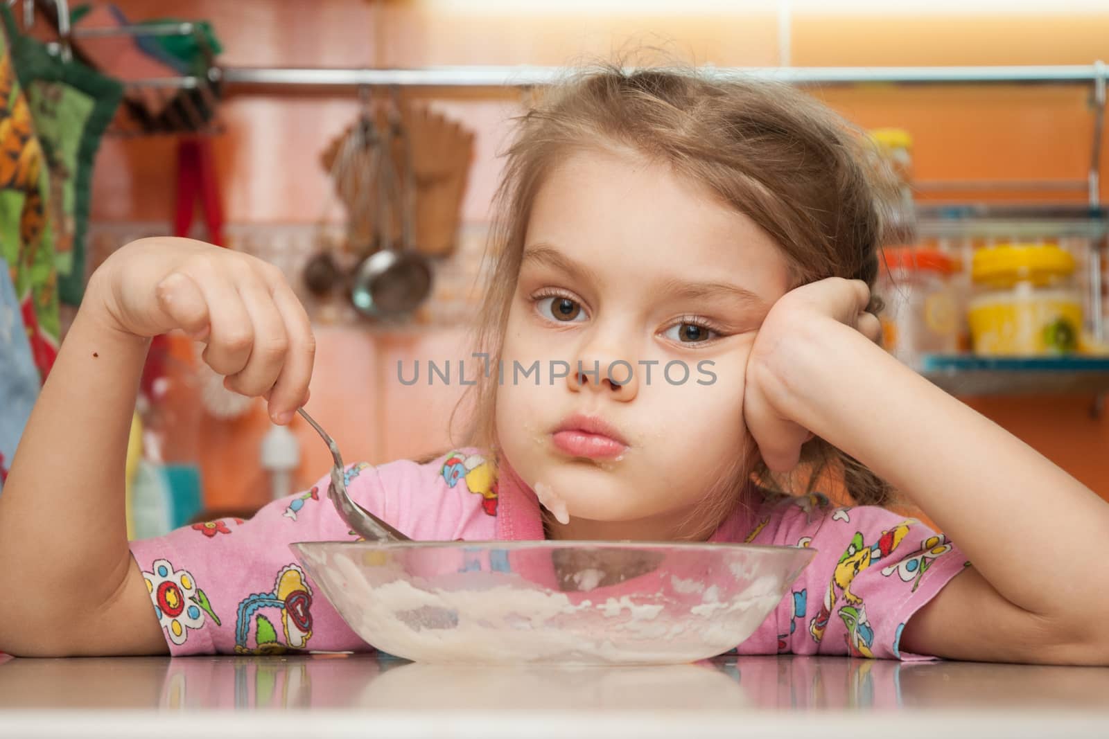 Sad five year old girl in the kitchen eating cereal