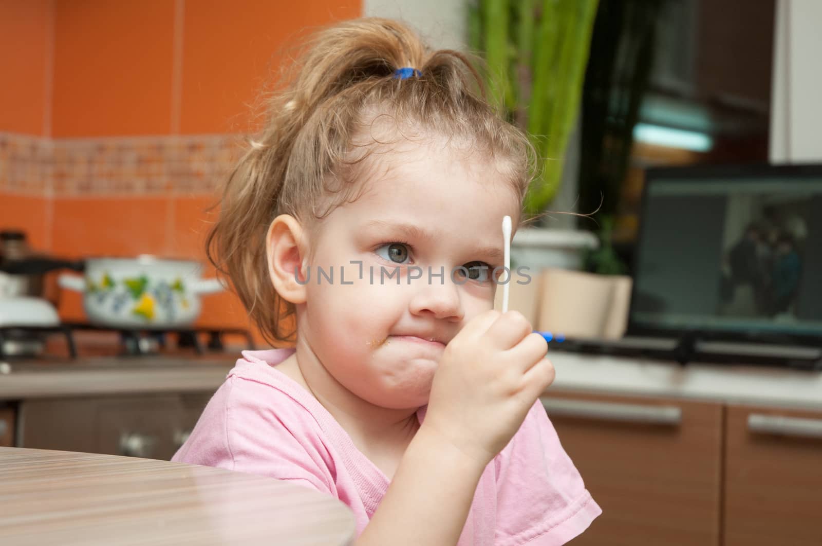 The three-year girl with a funny looking angrily at the cotton swab while sitting at the kitchen table