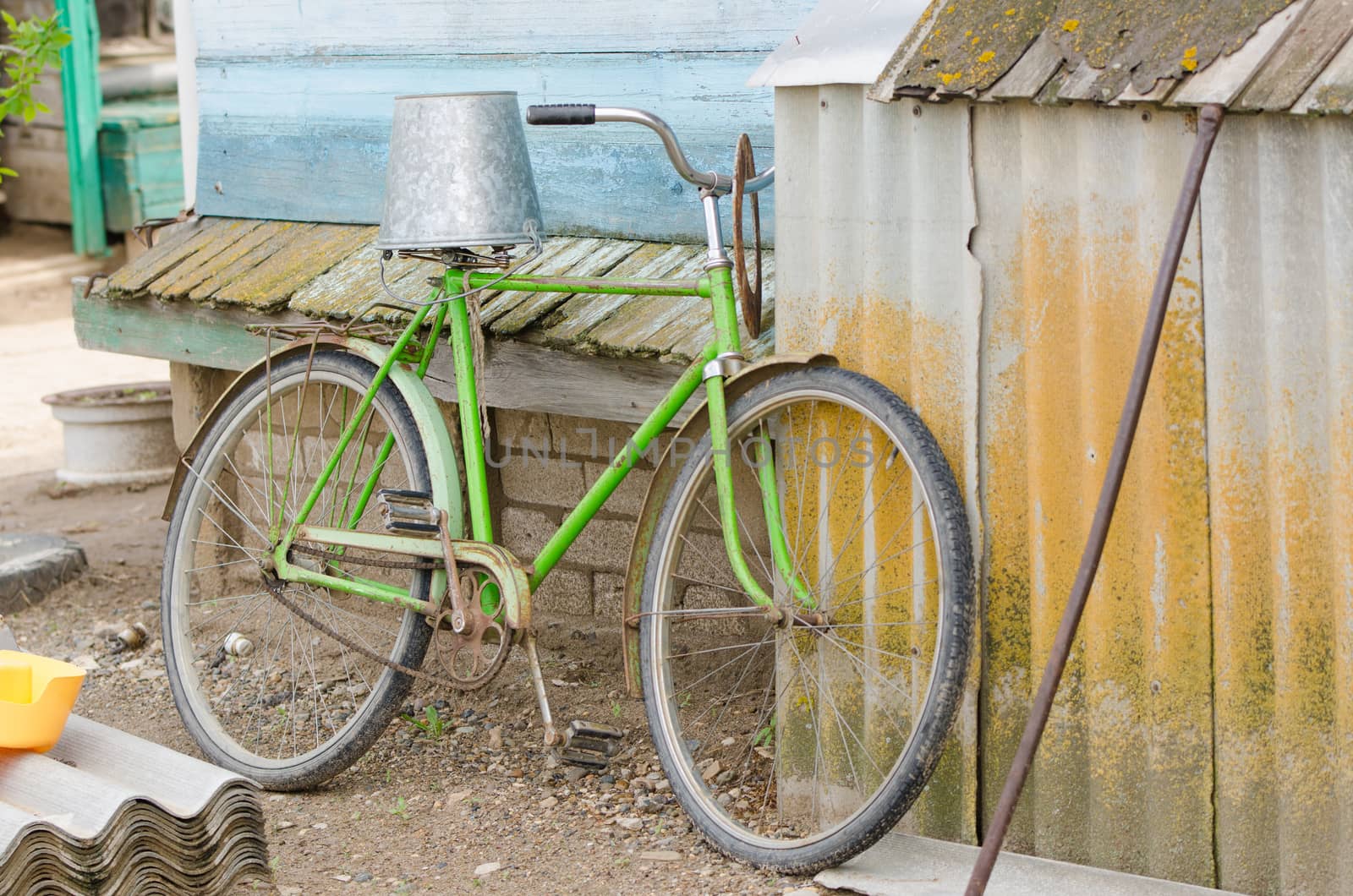 old bicycle with a bucket upside down on the saddle is at the wooden house