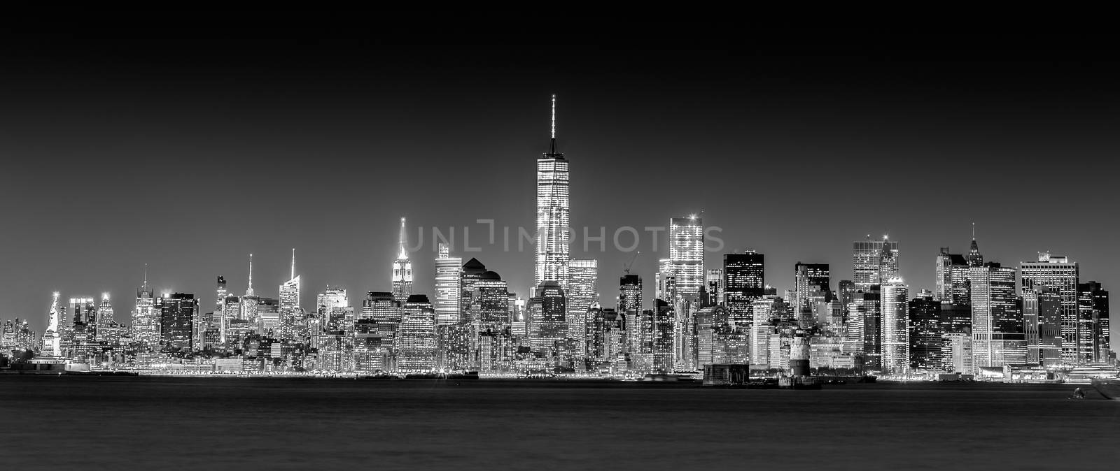 New York City Manhattan downtown skyline at dusk with skyscrapers illuminated over Hudson River panorama. Horizontal composition, copy space. Black and white image.