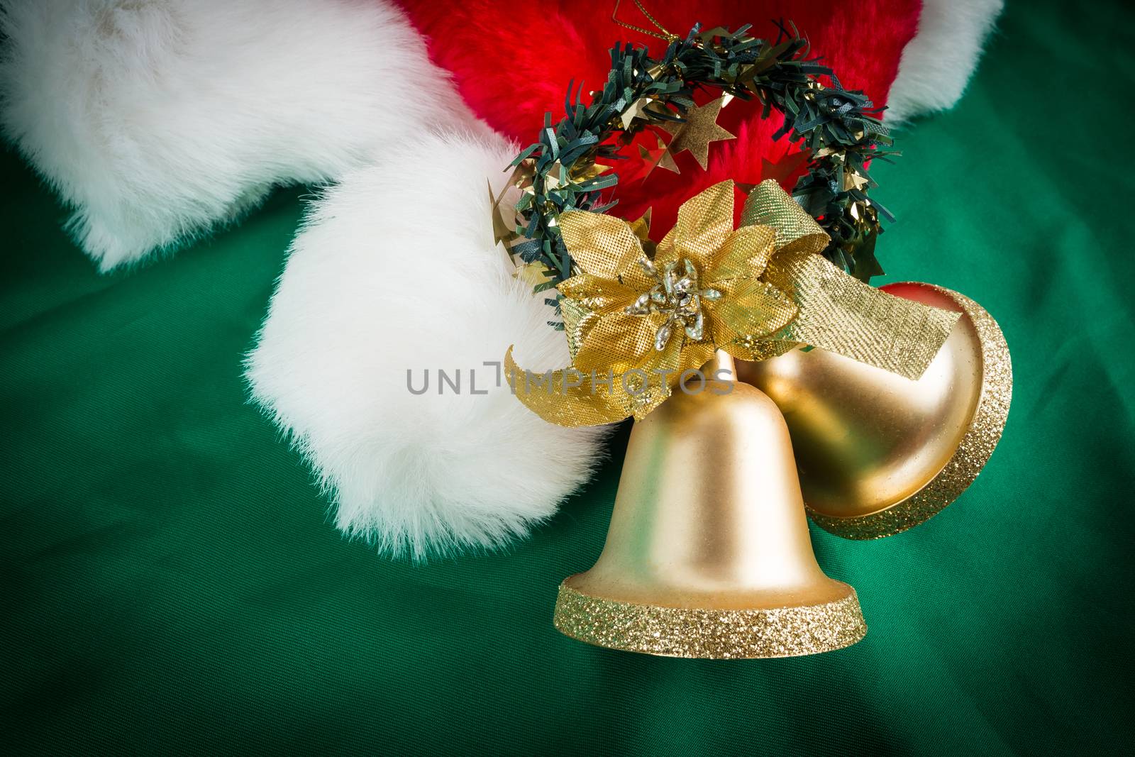 Santa Claus hat and gold bells on green cloth with dark vignette