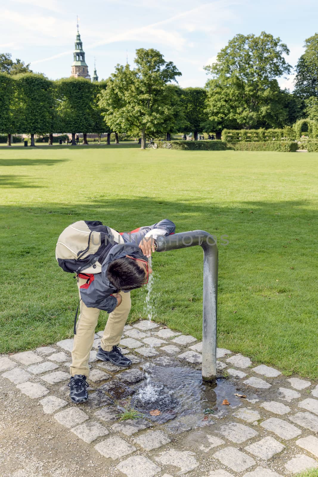 Boy getting a much needed drink from a water fountain in a park.