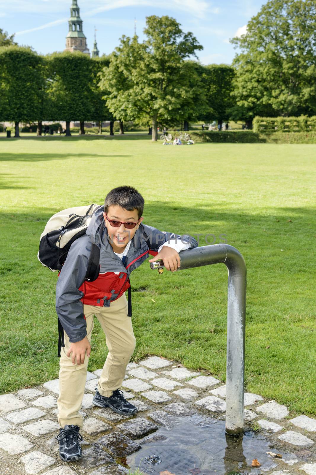 Boy getting a much needed drink from a water fountain in a park.