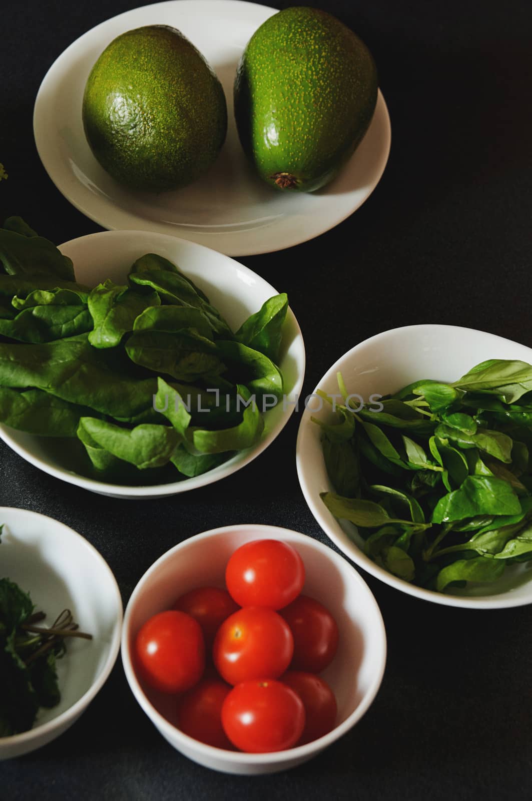 Plates with avocado, tomato and lettuce on dark background